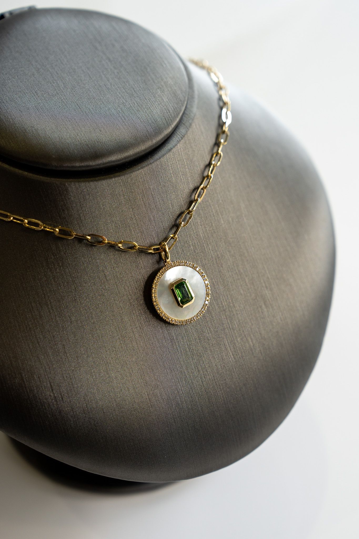 Gold necklace with a green stone pendant on a black display bust.