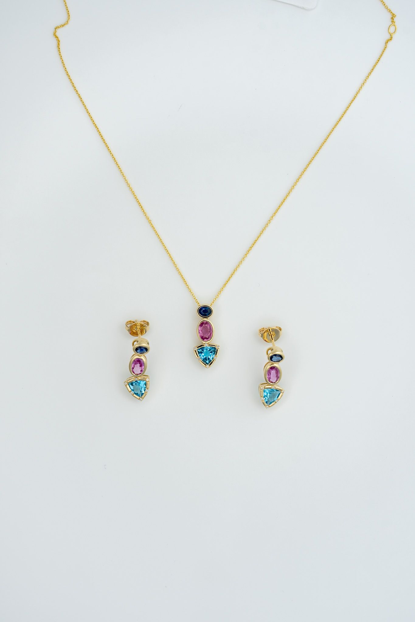 Gold necklace with colorful gemstone pendant and matching stud earrings on a white background.