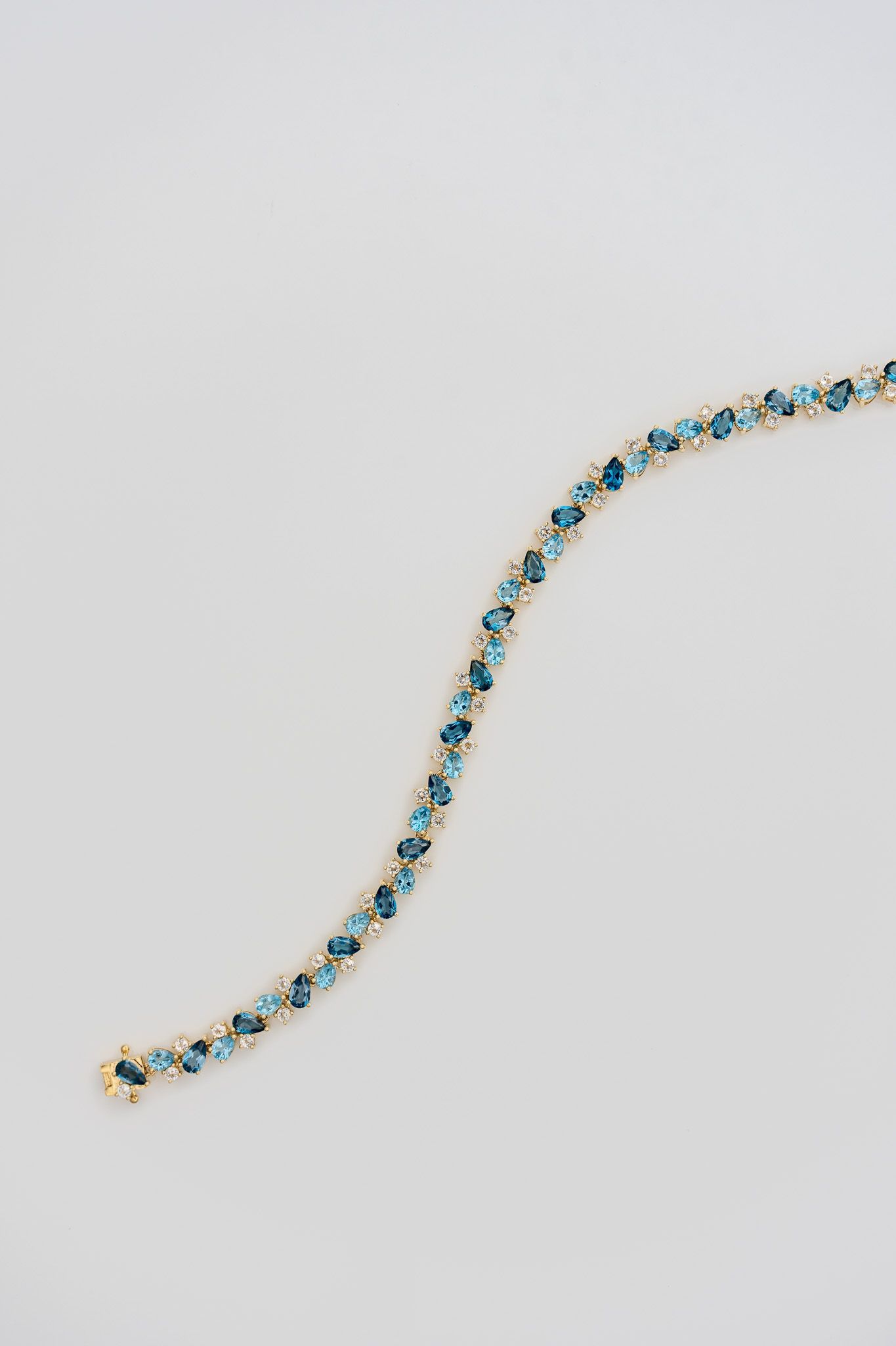 Delicate blue and gold beaded chain curved on a light gray background.