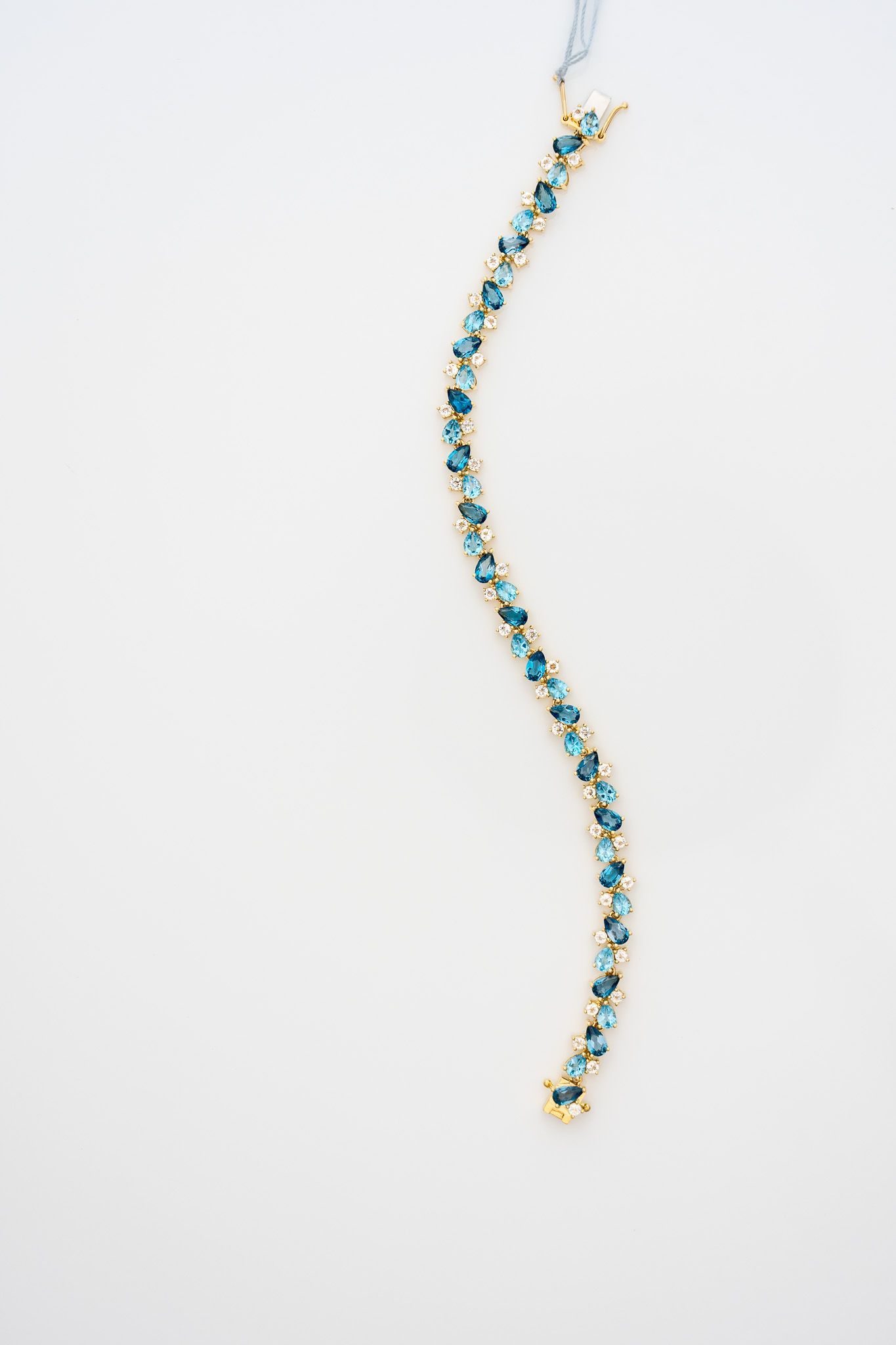 Delicate gold bracelet with blue stones, curved vertically on a white background.