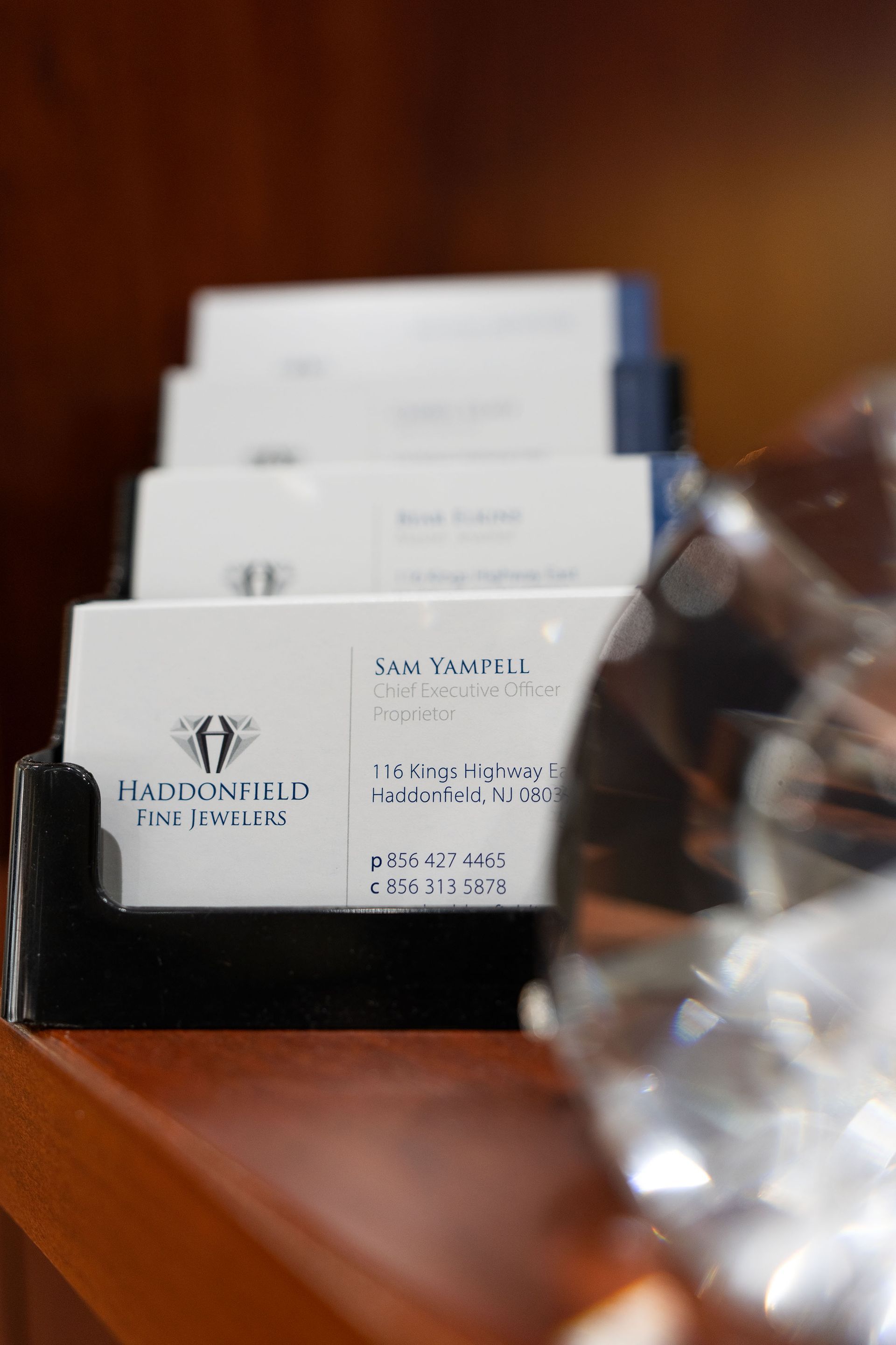 Business cards in a black holder on a wooden desk, with a blurred clear glass object at right.