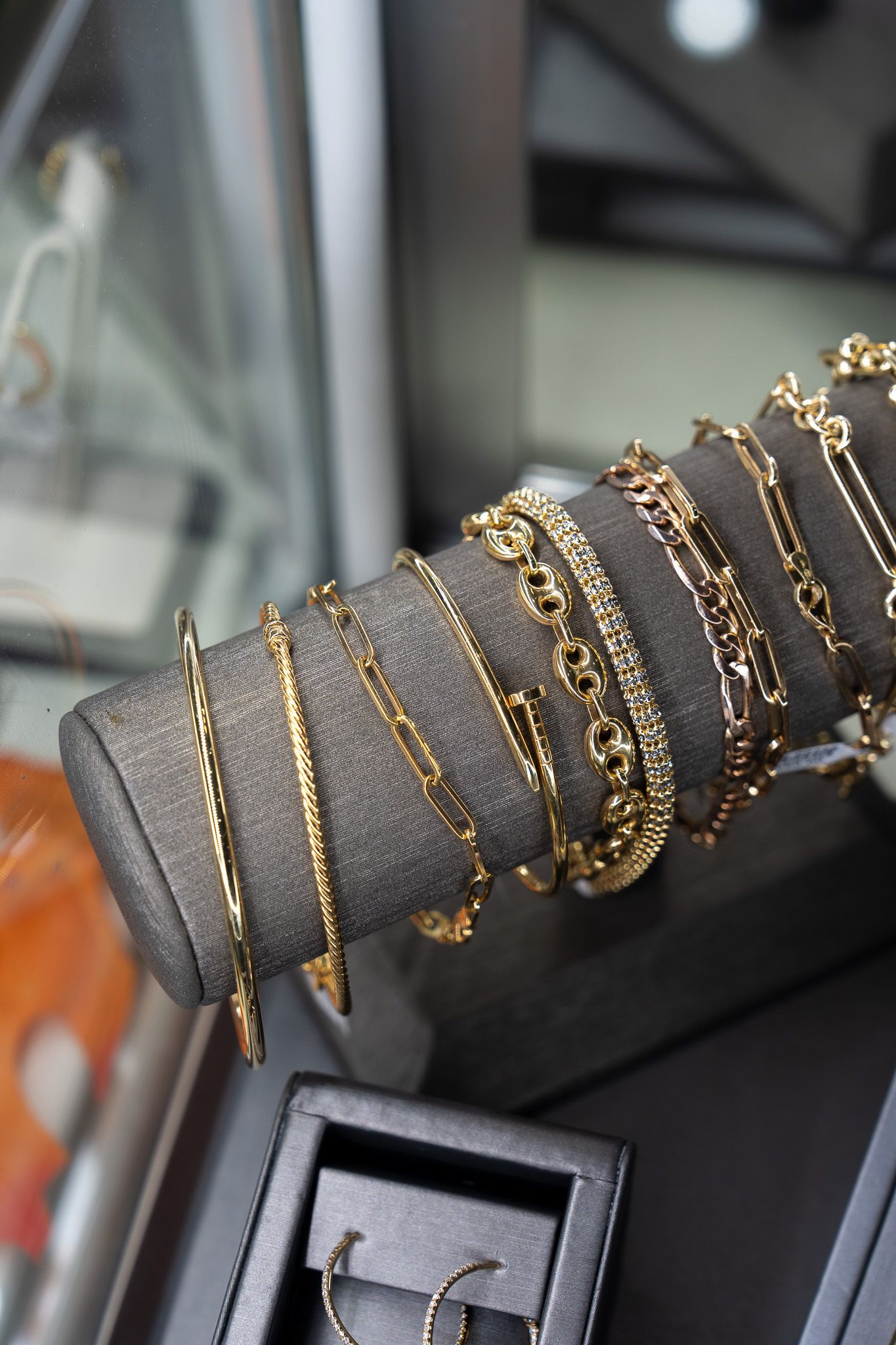 Gold bracelets stacked on a gray velvet jewelry display stand in a store window.