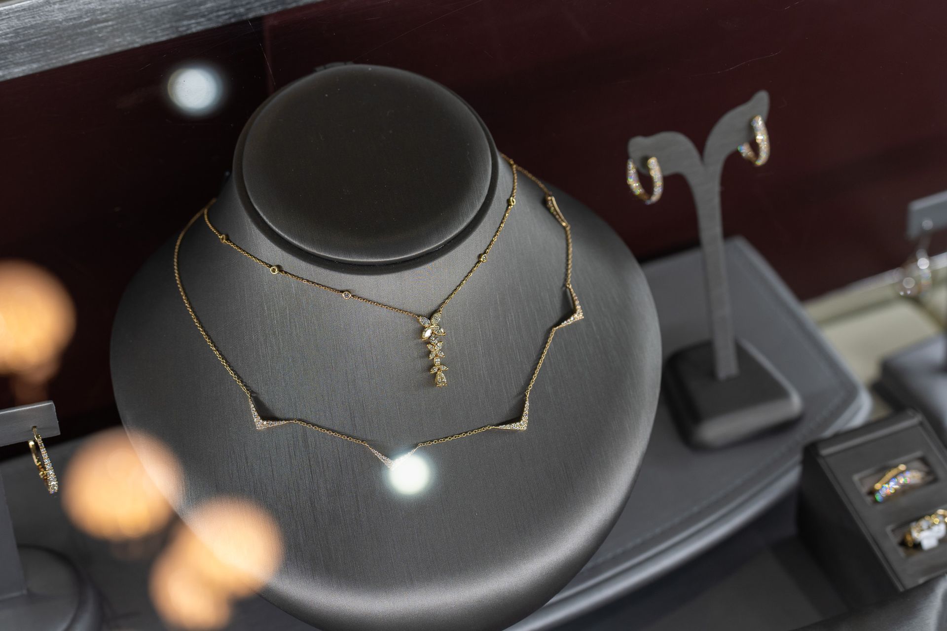 Gold necklace on a black display bust in a jewelry store showcase.