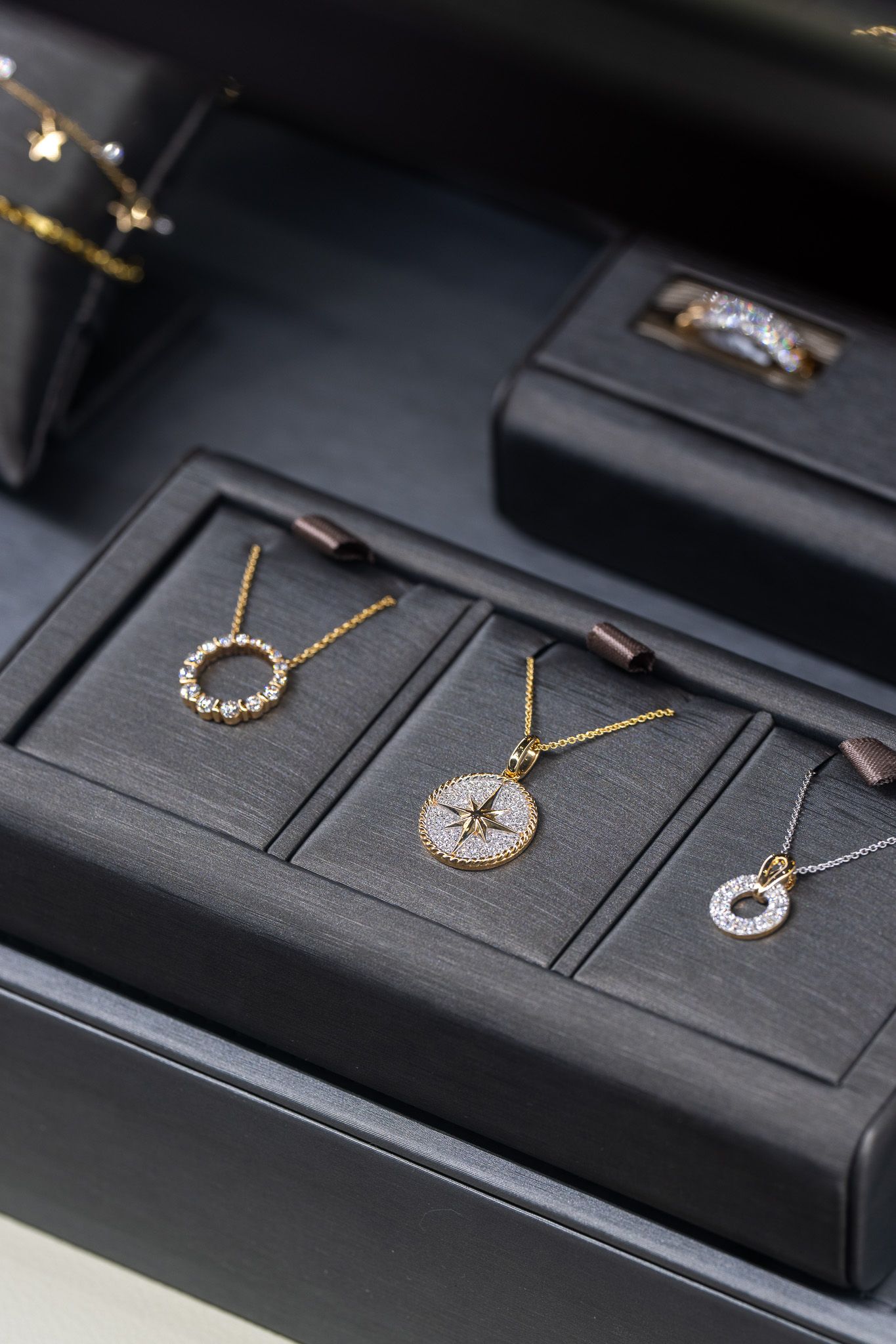 Three gold necklaces displayed in a black jewelry box with matching rings on dark fabric.