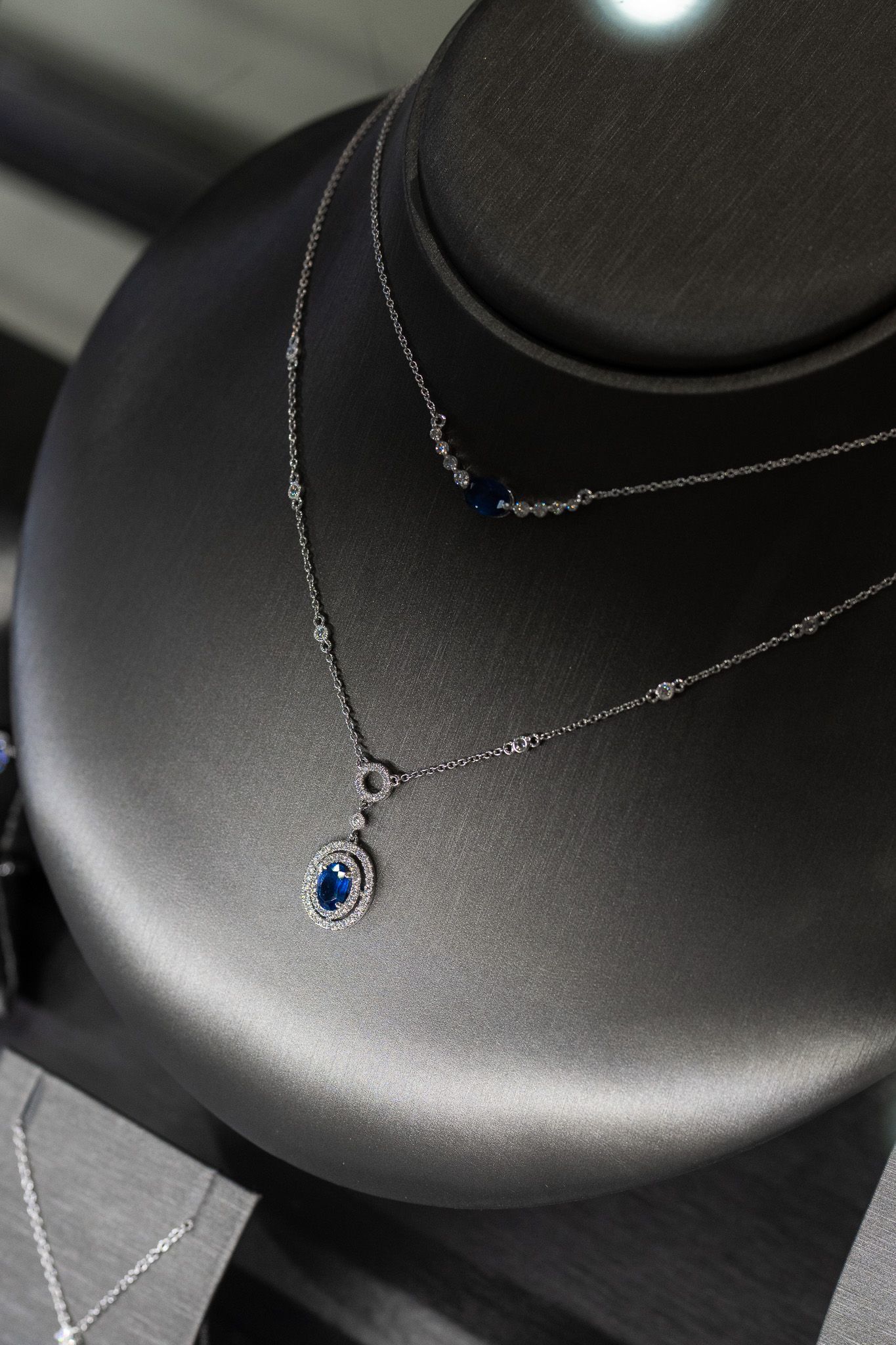 Two layered silver necklaces on a black display bust, including a small blue pendant.