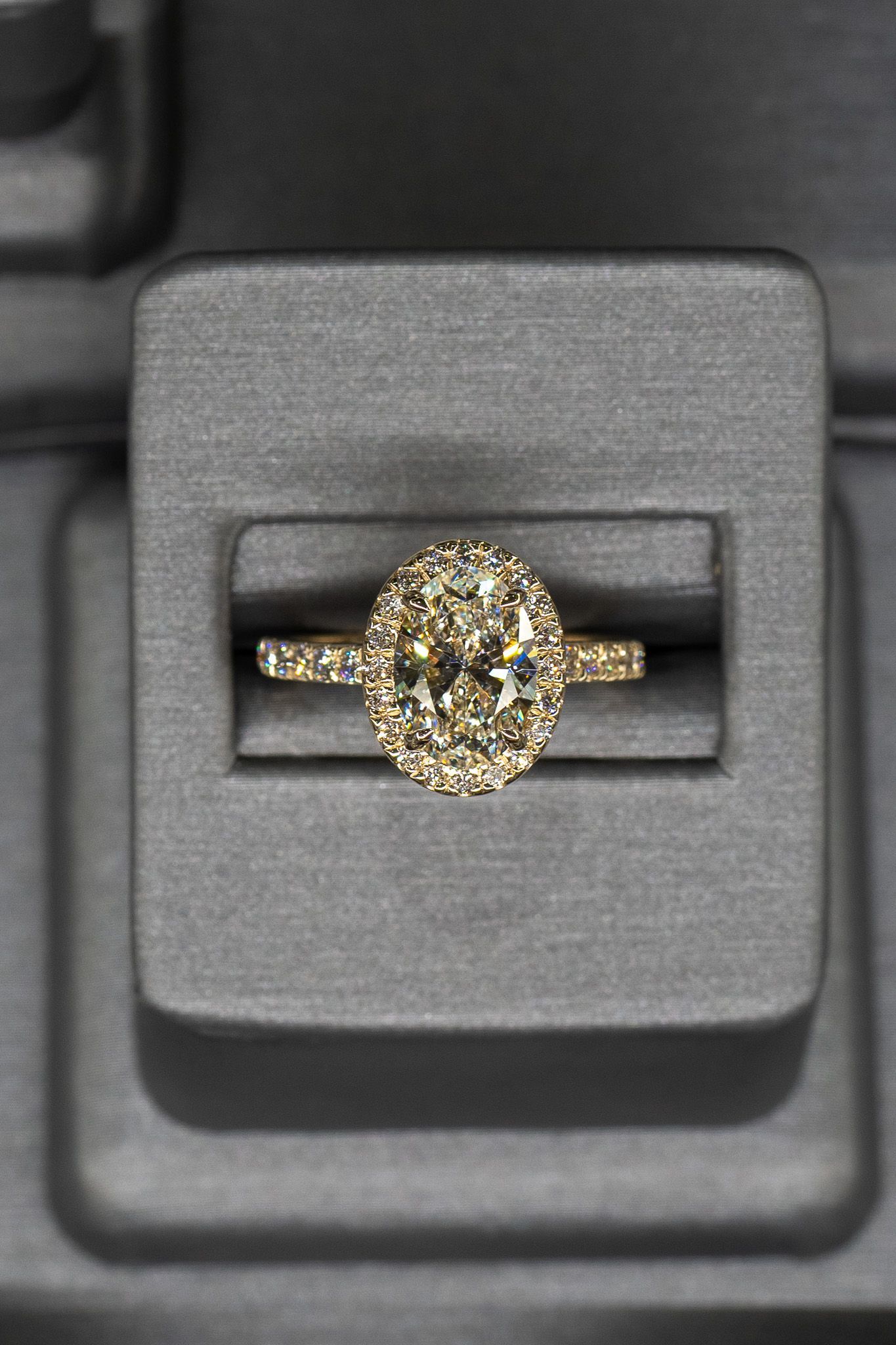 Gold ring with a round cluster setting displayed in a dark jewelry box.