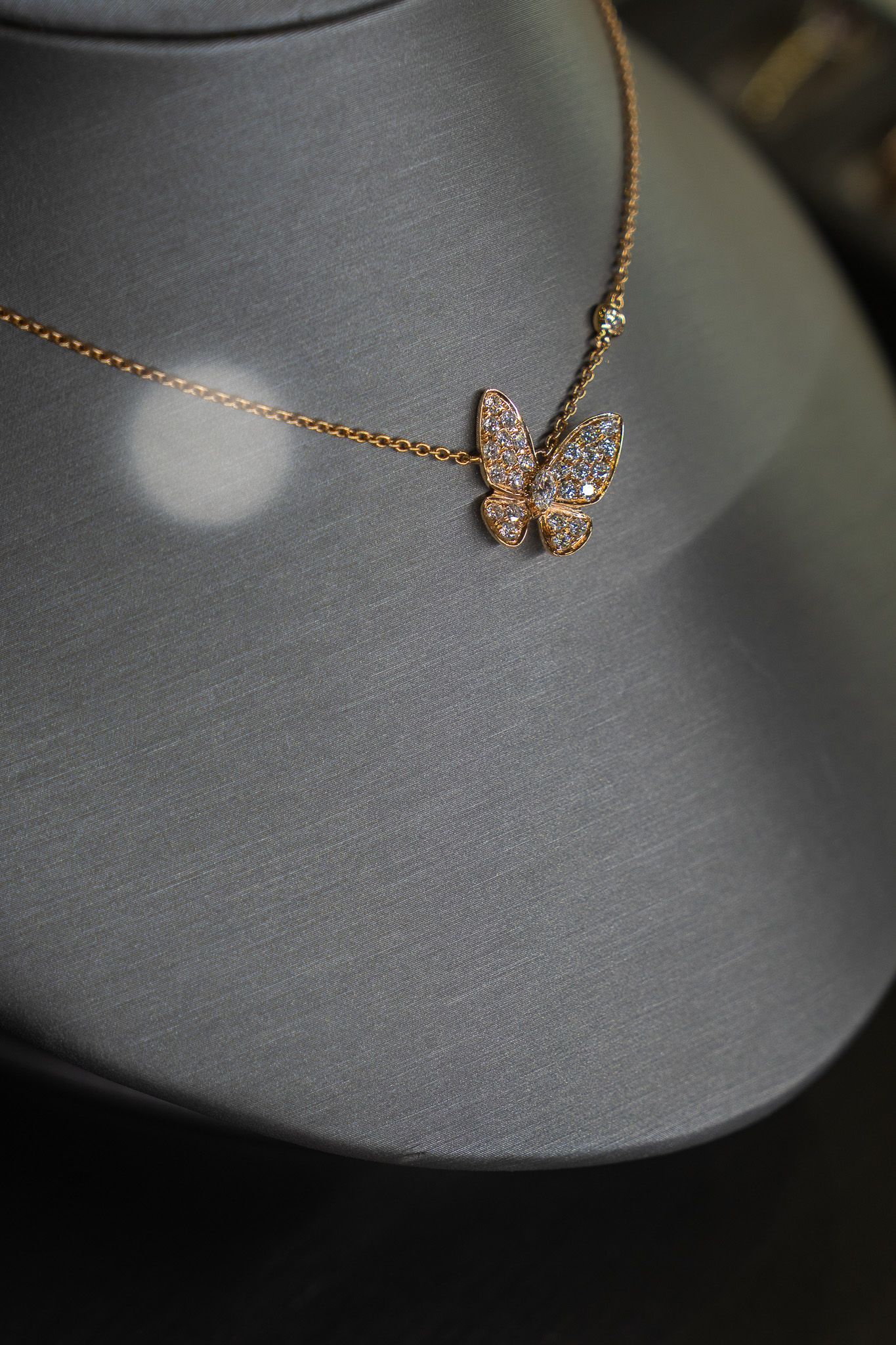Gold butterfly pendant necklace on a gray display bust.
