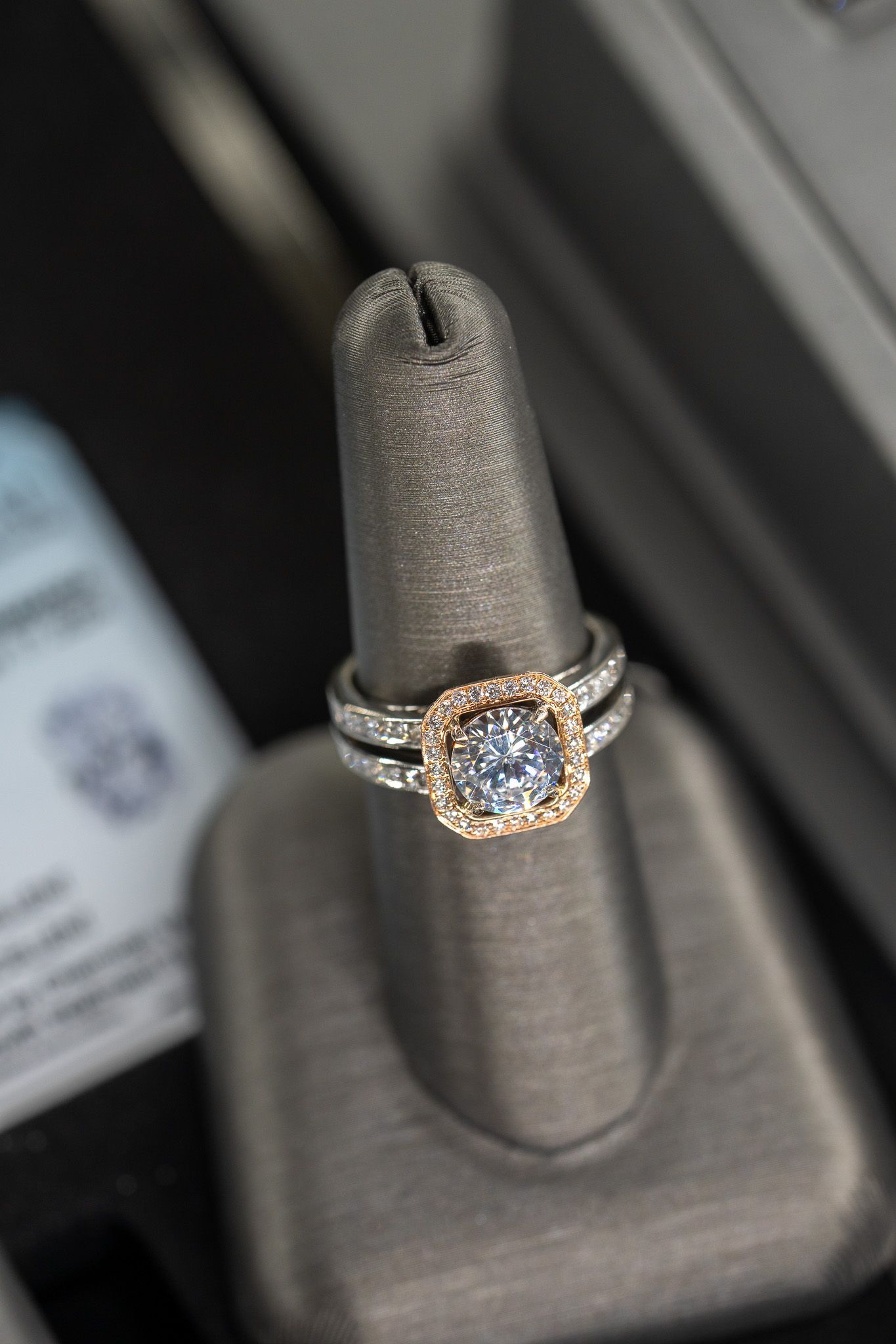 Gold-and-silver engagement ring displayed on a gray jewelry stand.