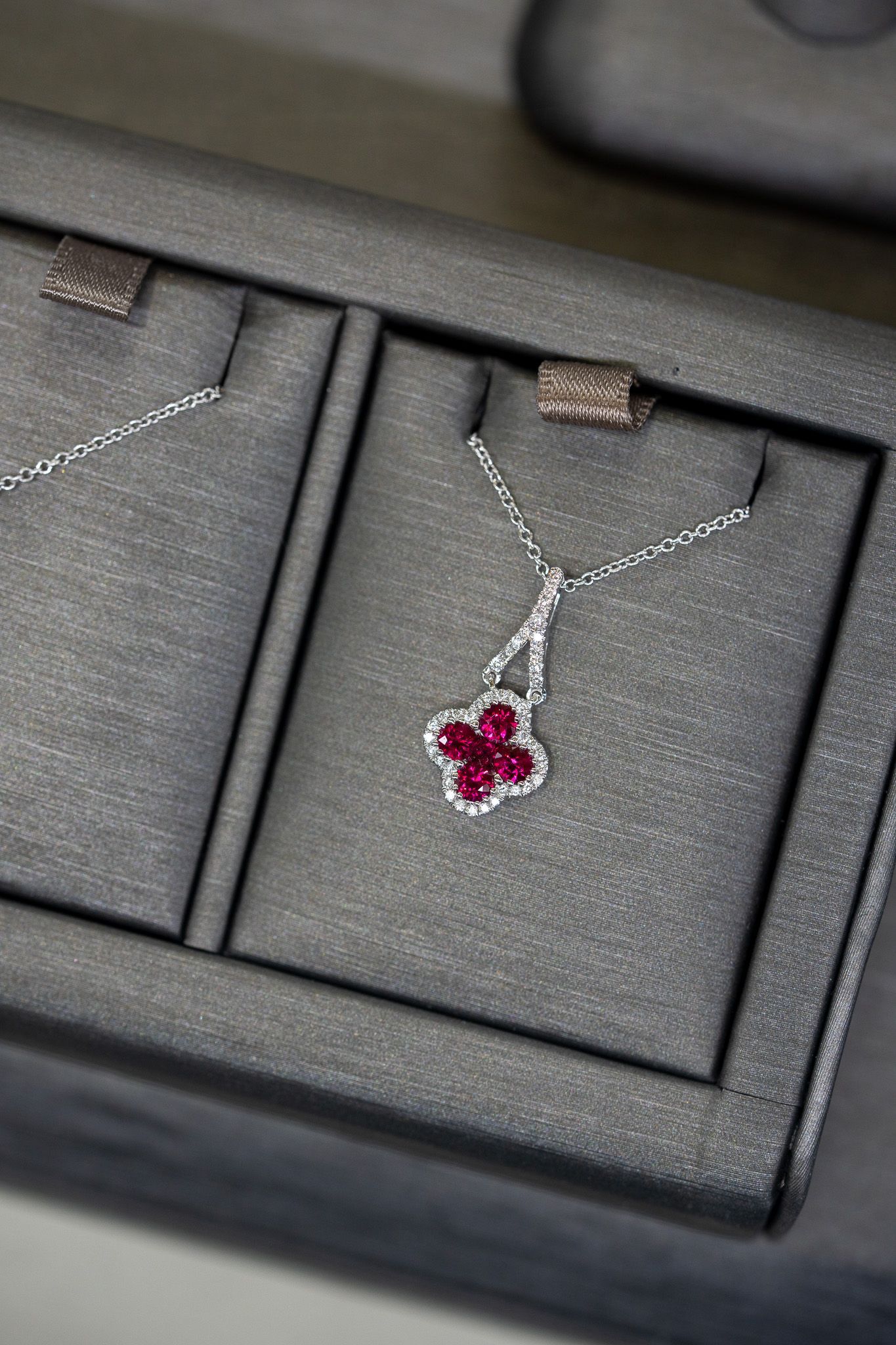 Two silver heart necklaces with pink gemstone pendants in a display box.
