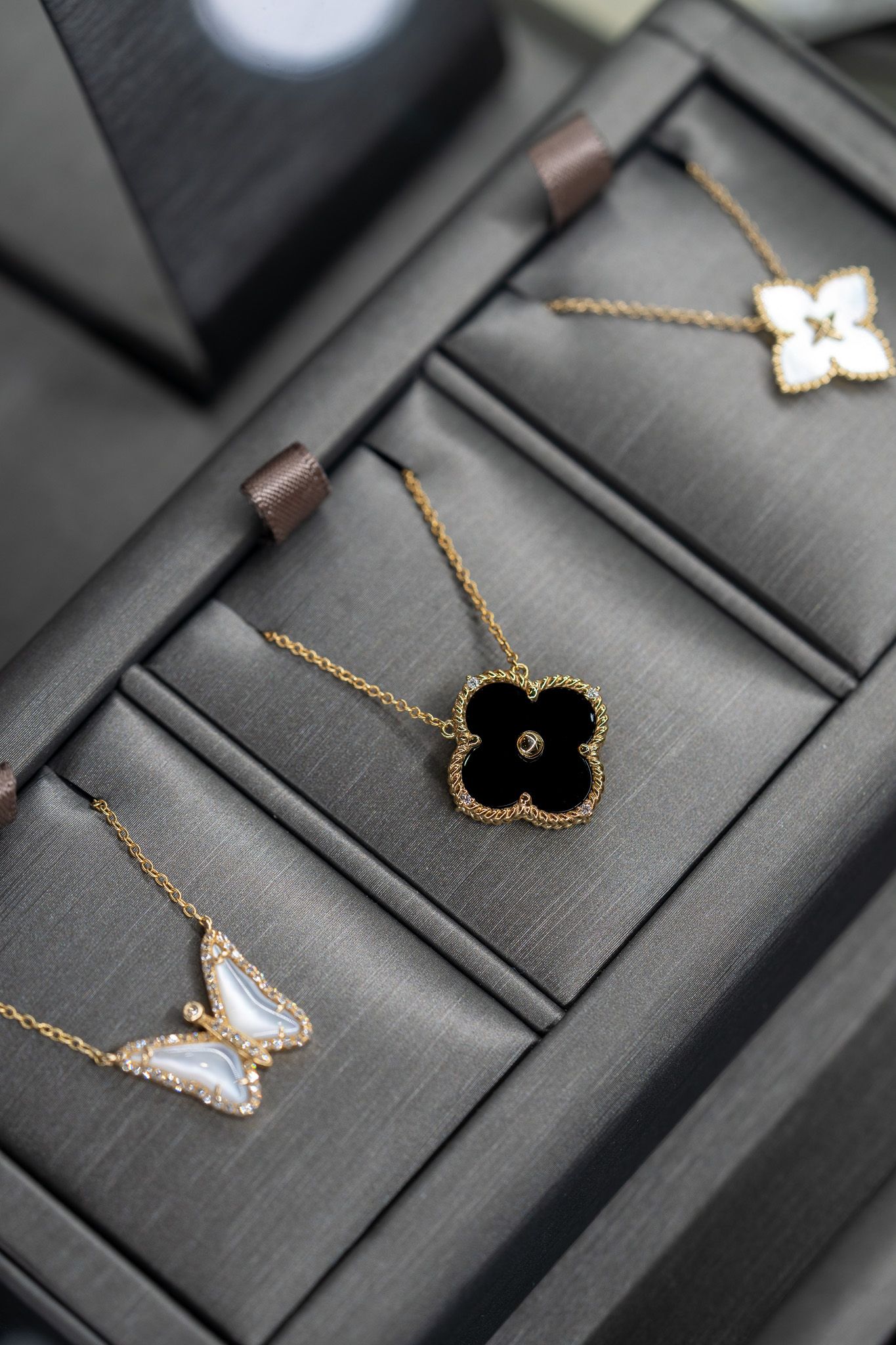 Three delicate necklaces with flower pendants on black jewelry displays.