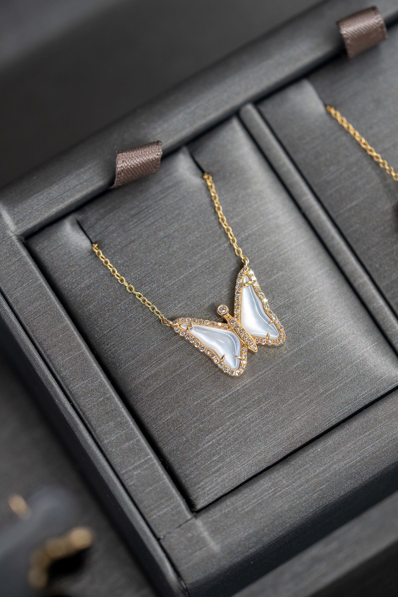 Butterfly pendant necklace with gold and white stones in a black jewelry box.