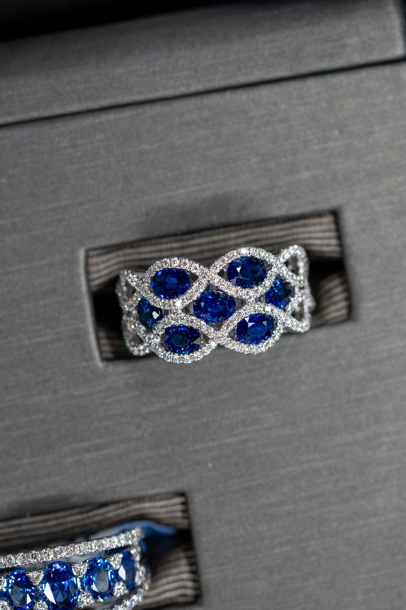 Silver ring with blue stones in an interlaced pattern on a dark display tray.