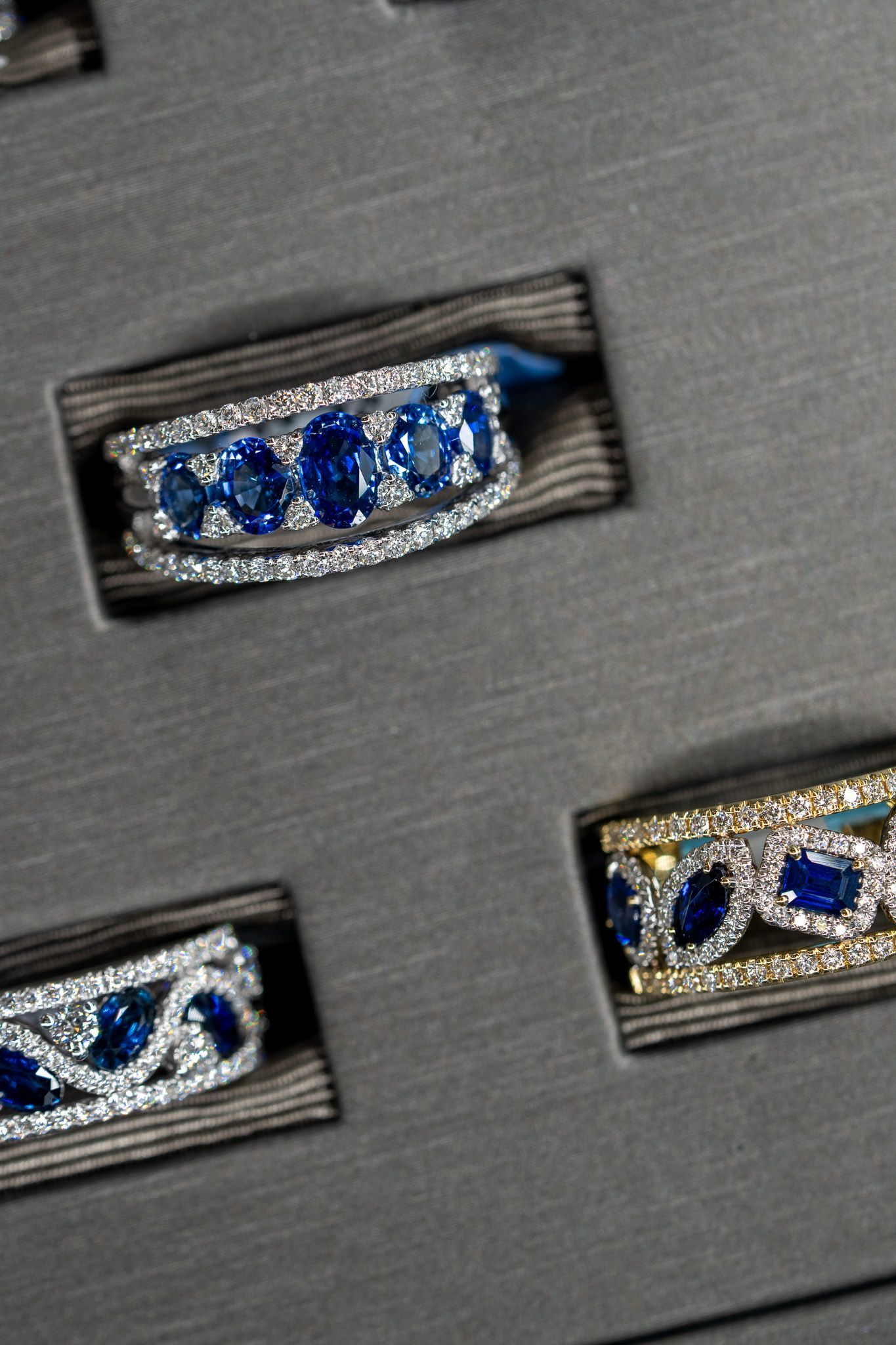 Close-up of three silver rings with blue gemstones on a dark gray display background.