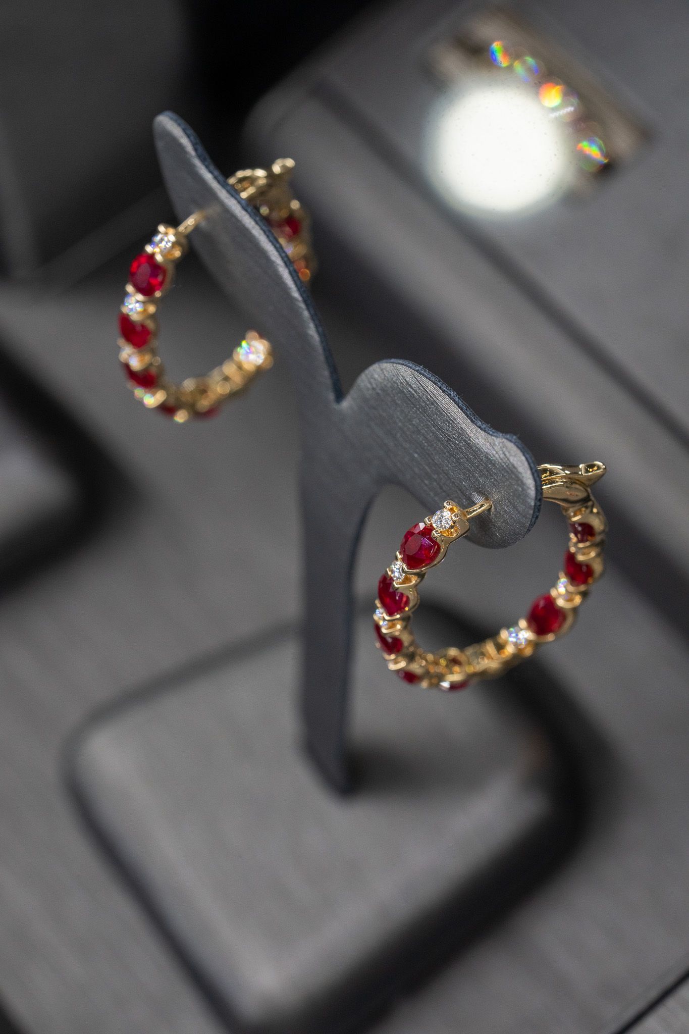 Red and gold hoop earrings displayed on a gray jewelry stand.