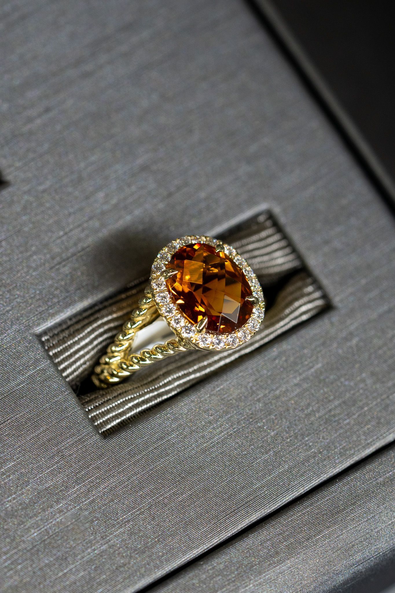 Gold ring with an oval amber gemstone on a gray textured display box.