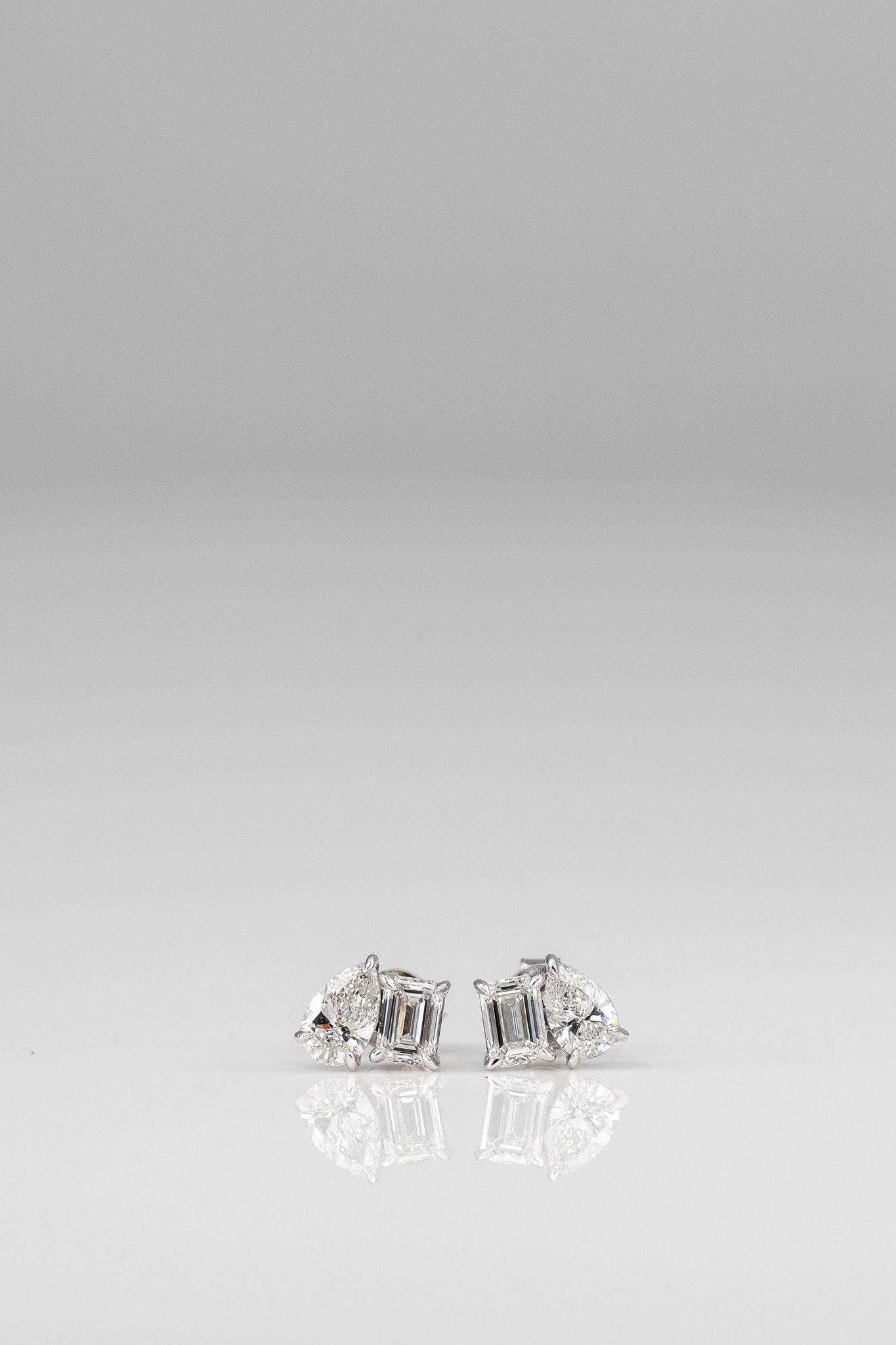 Two small silver decorative objects on a white surface, with soft reflections and a plain gray background