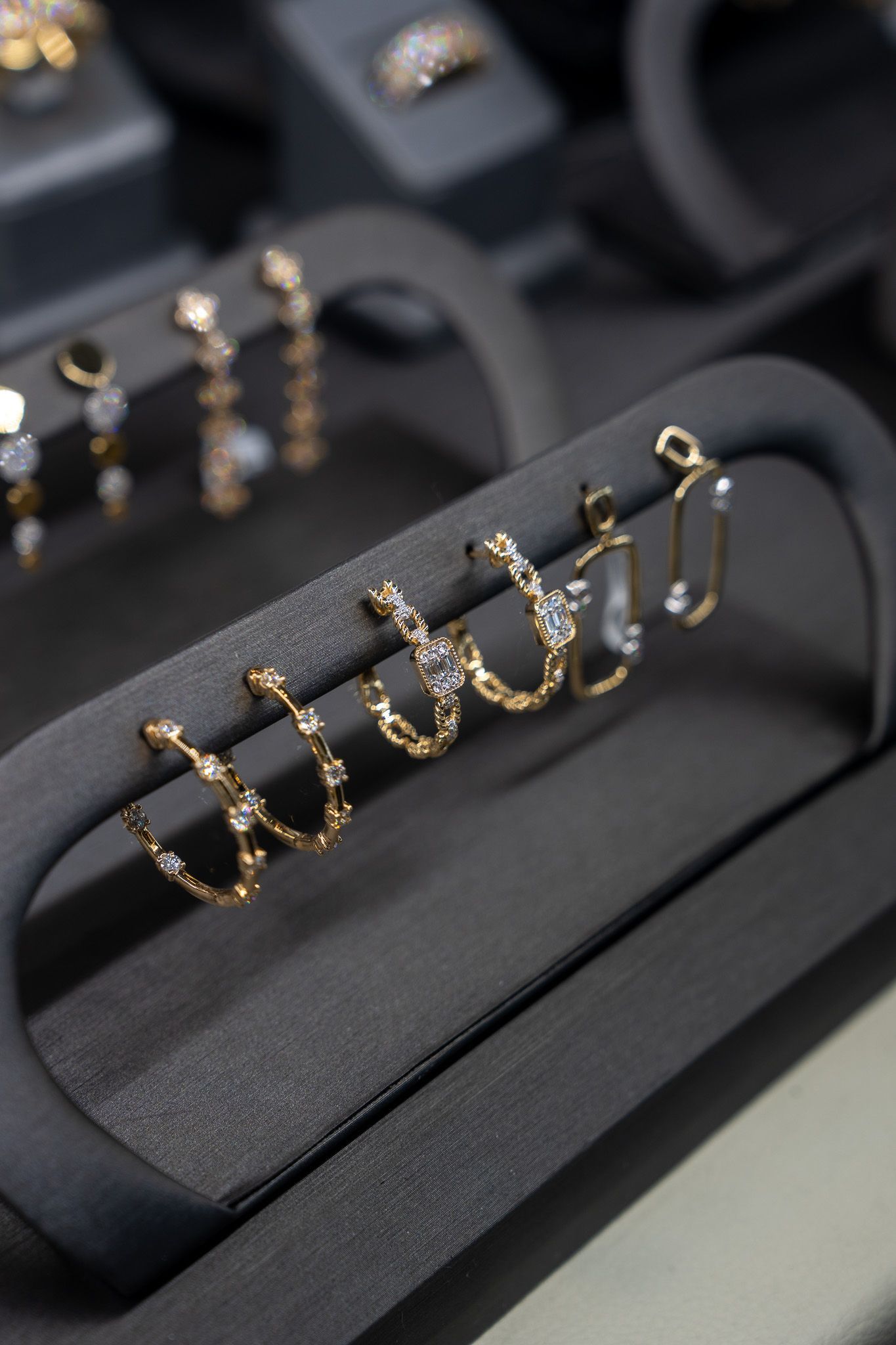 Gold hoop earrings displayed on a black jewelry stand, with several pairs lined up in the background