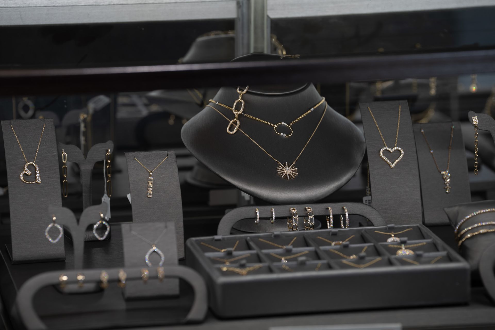 Jewelry display with silver and gold necklaces, bracelets, and rings on black stands and trays.