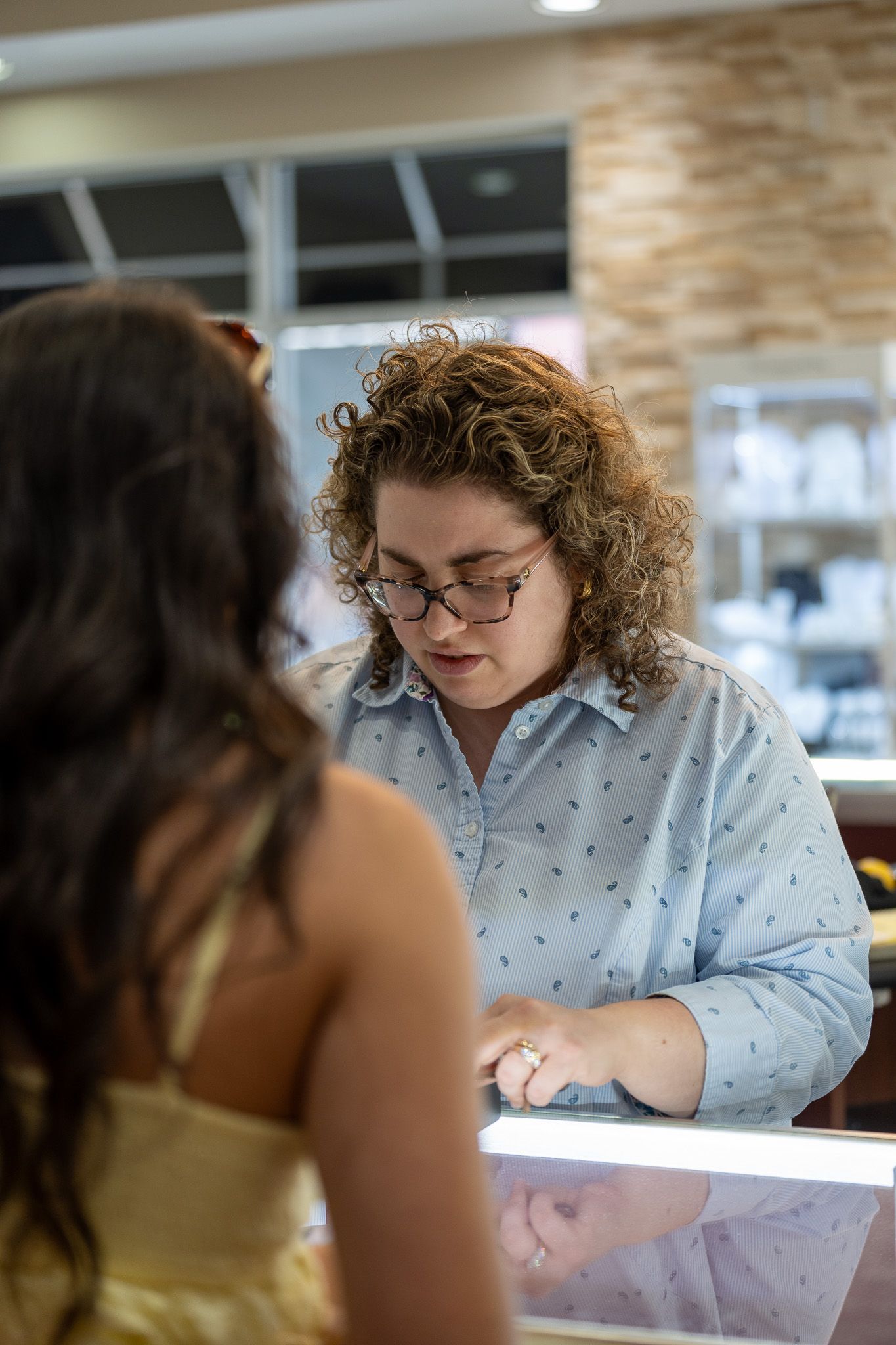 Customer service desk with a curly-haired person in a blue shirt assisting a customer in a bright store