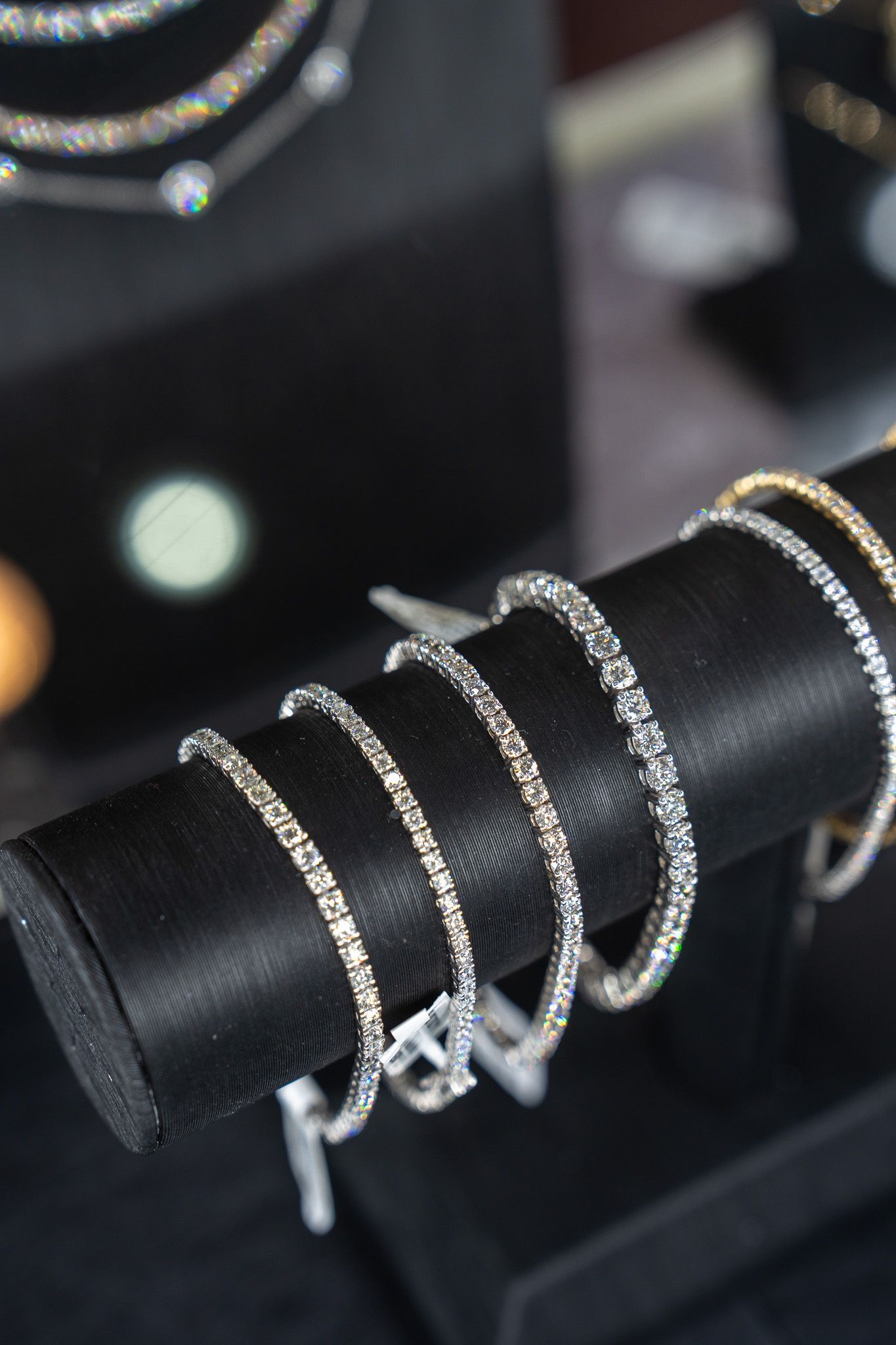 Silver chain bracelets on a black cylindrical display stand in a jewelry case
