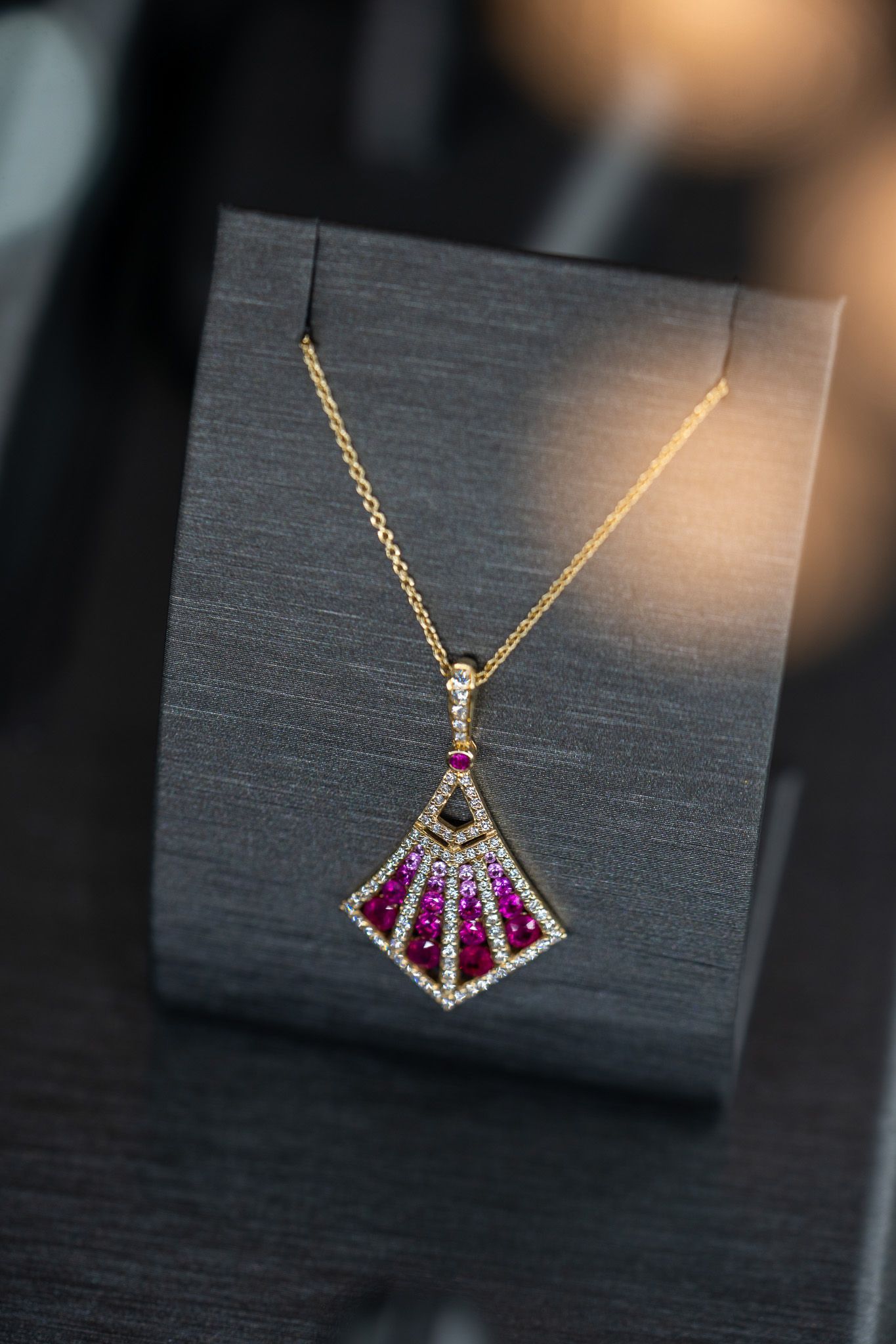 Gold necklace with a pink gemstone pendant displayed on a black stand.