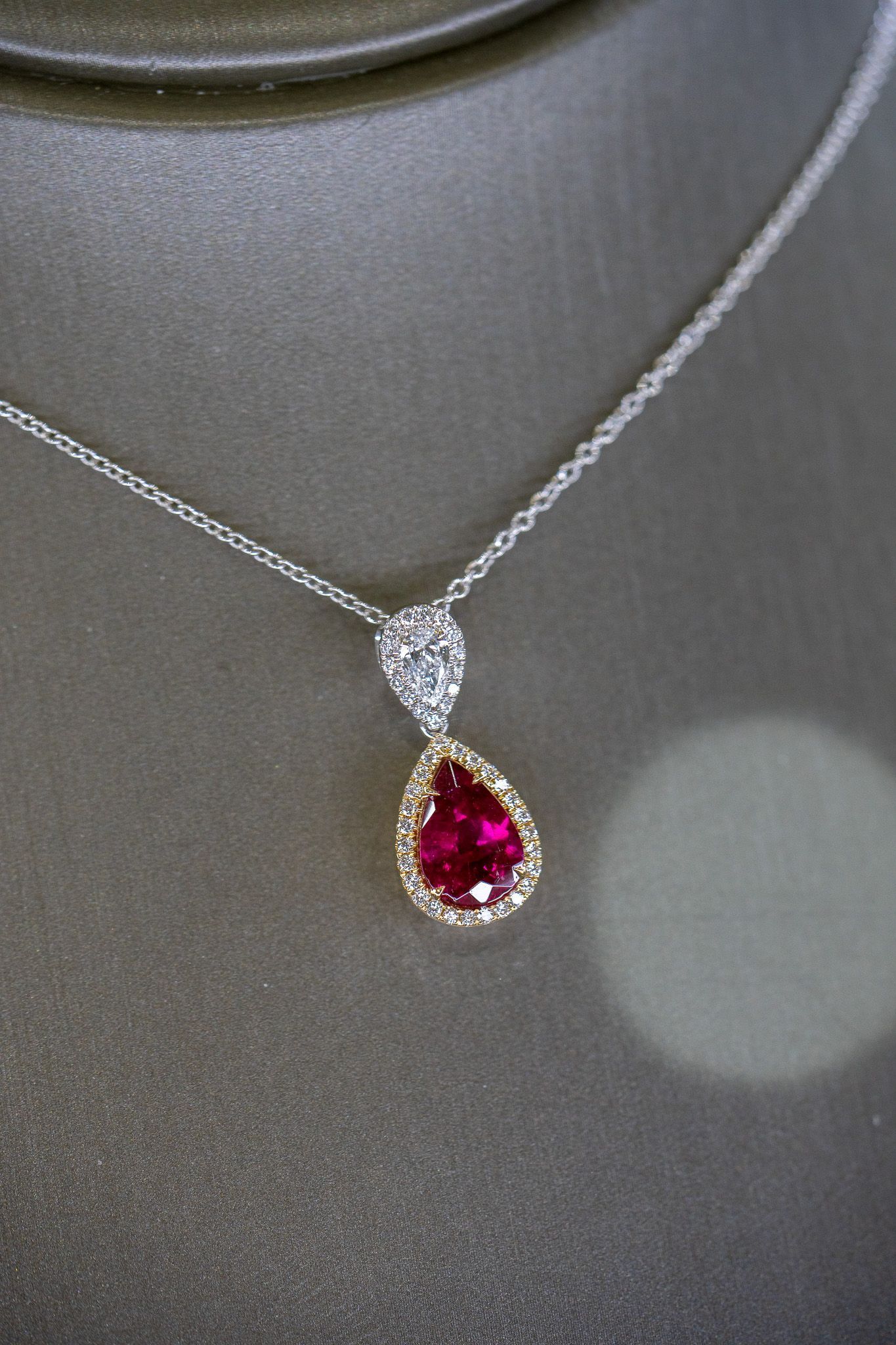 Silver necklace with a pear-shaped red gemstone pendant on a dark display background.