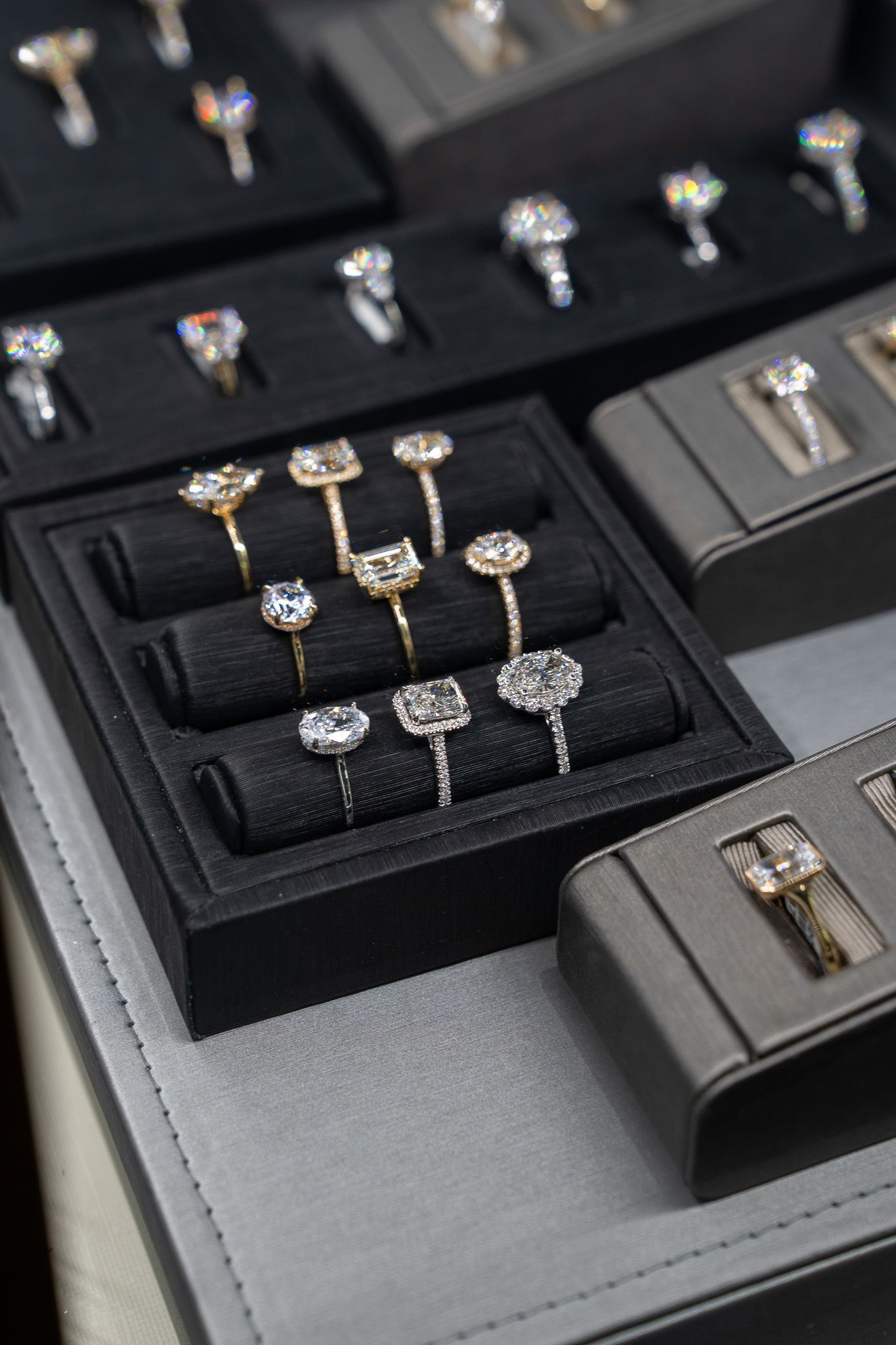 Assorted diamond rings displayed in black jewelry trays on a gray surface
