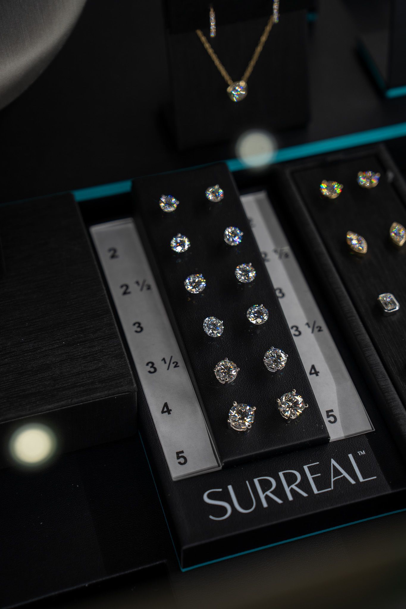 Black jewelry display with silver pieces, ruler, and “SURREAL” label