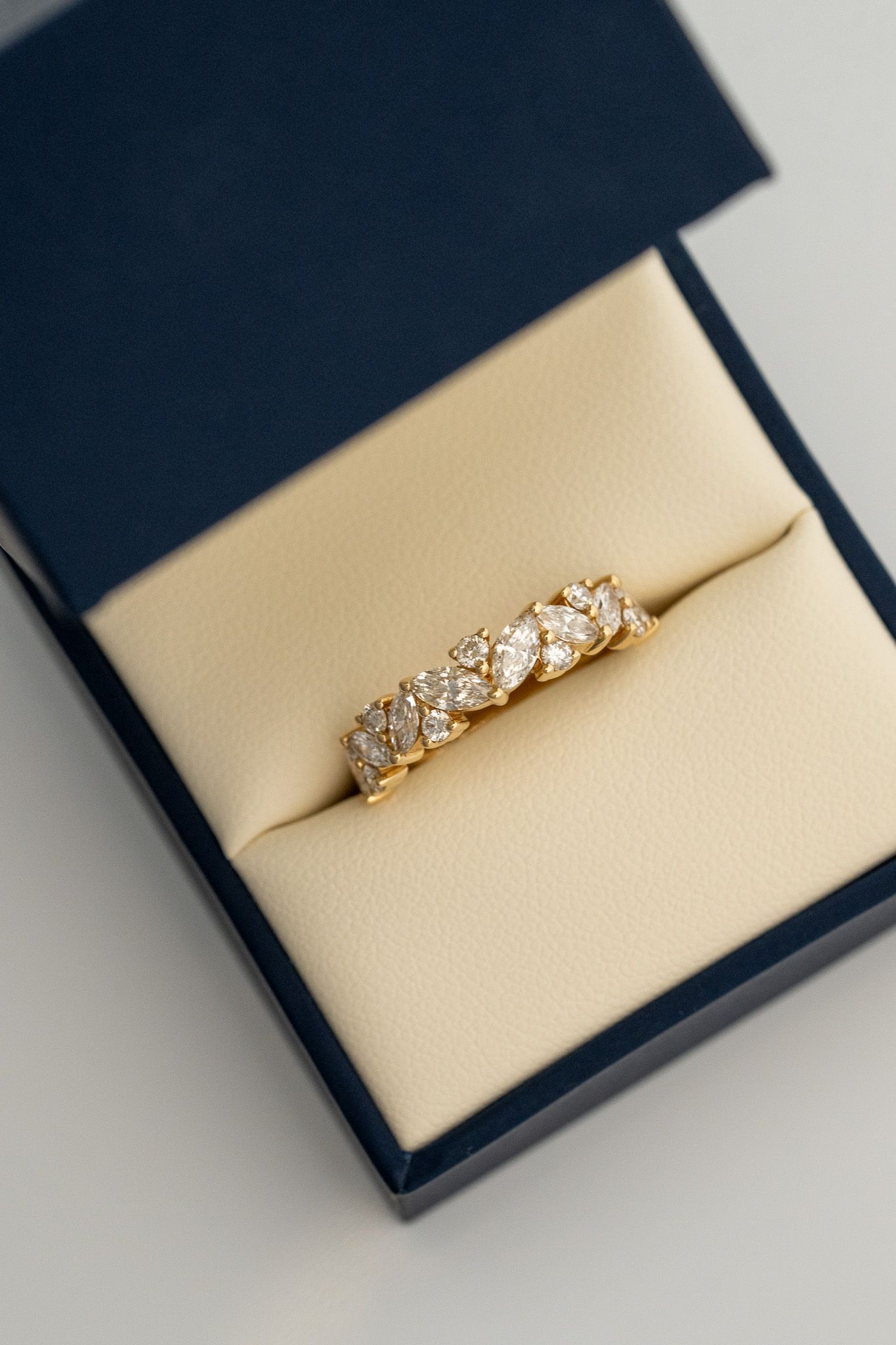 Gold diamond ring in a navy jewelry box with a beige cushion.