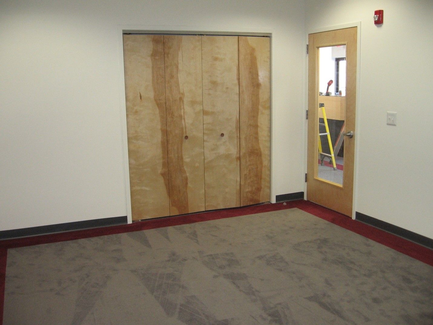 An newly constructed empty room with a wooden door and a carpeted floor