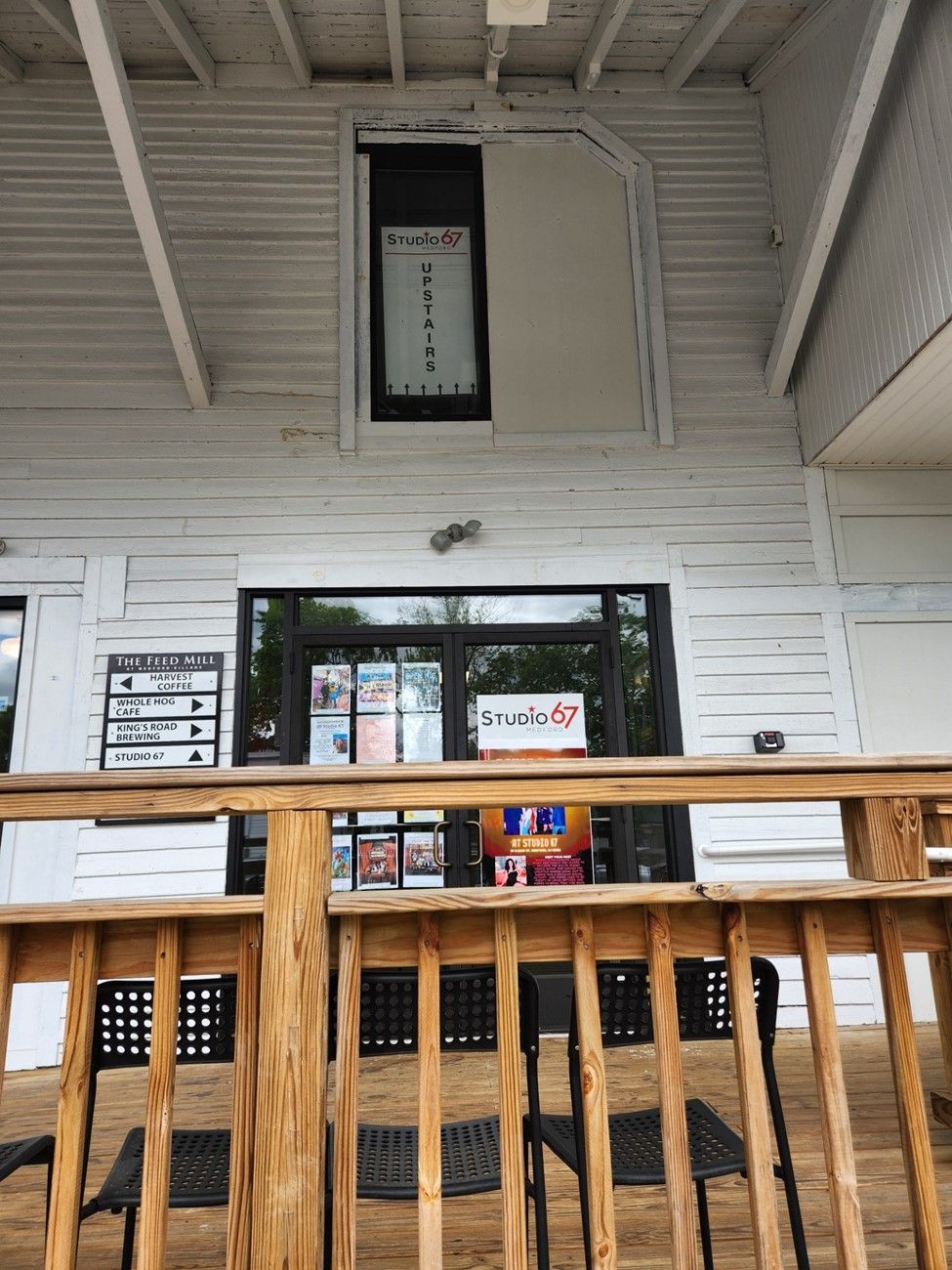 A wooden deck with tables and chairs in front of the feed mill.