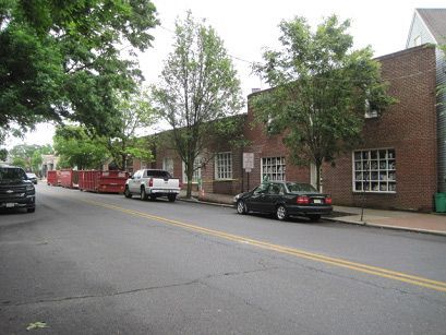 A black car is parked on the side of the road in front of a brick building.