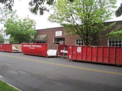 A row of red dumpsters are parked in front of a brick building