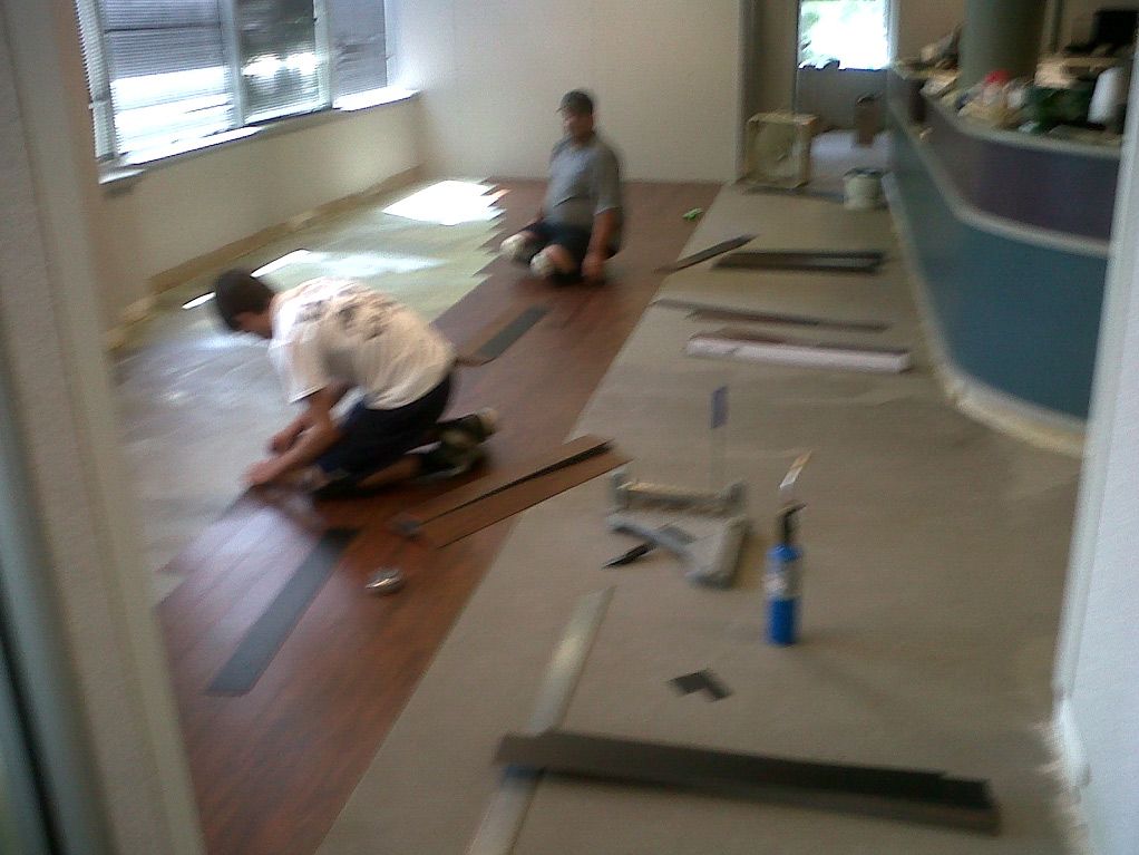 Two men are working on a wooden floor in a room