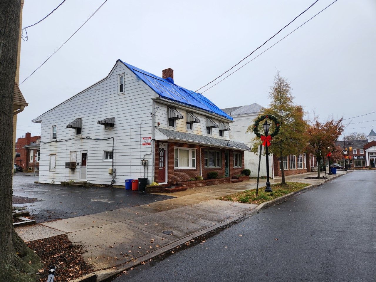 A white house with a blue roof is sitting on the corner of a street.