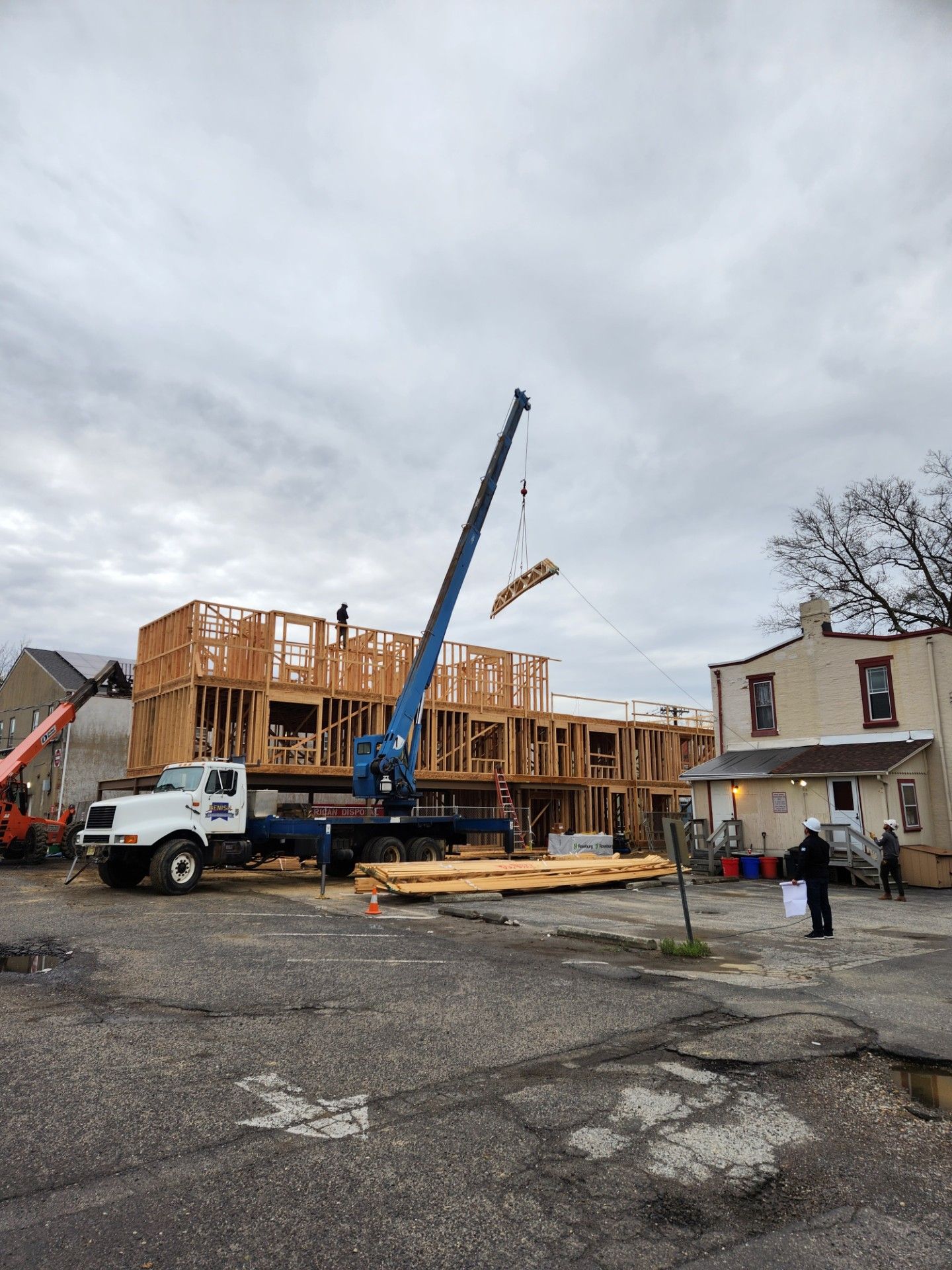 A crane is lifting a piece of wood in front of a building under construction.