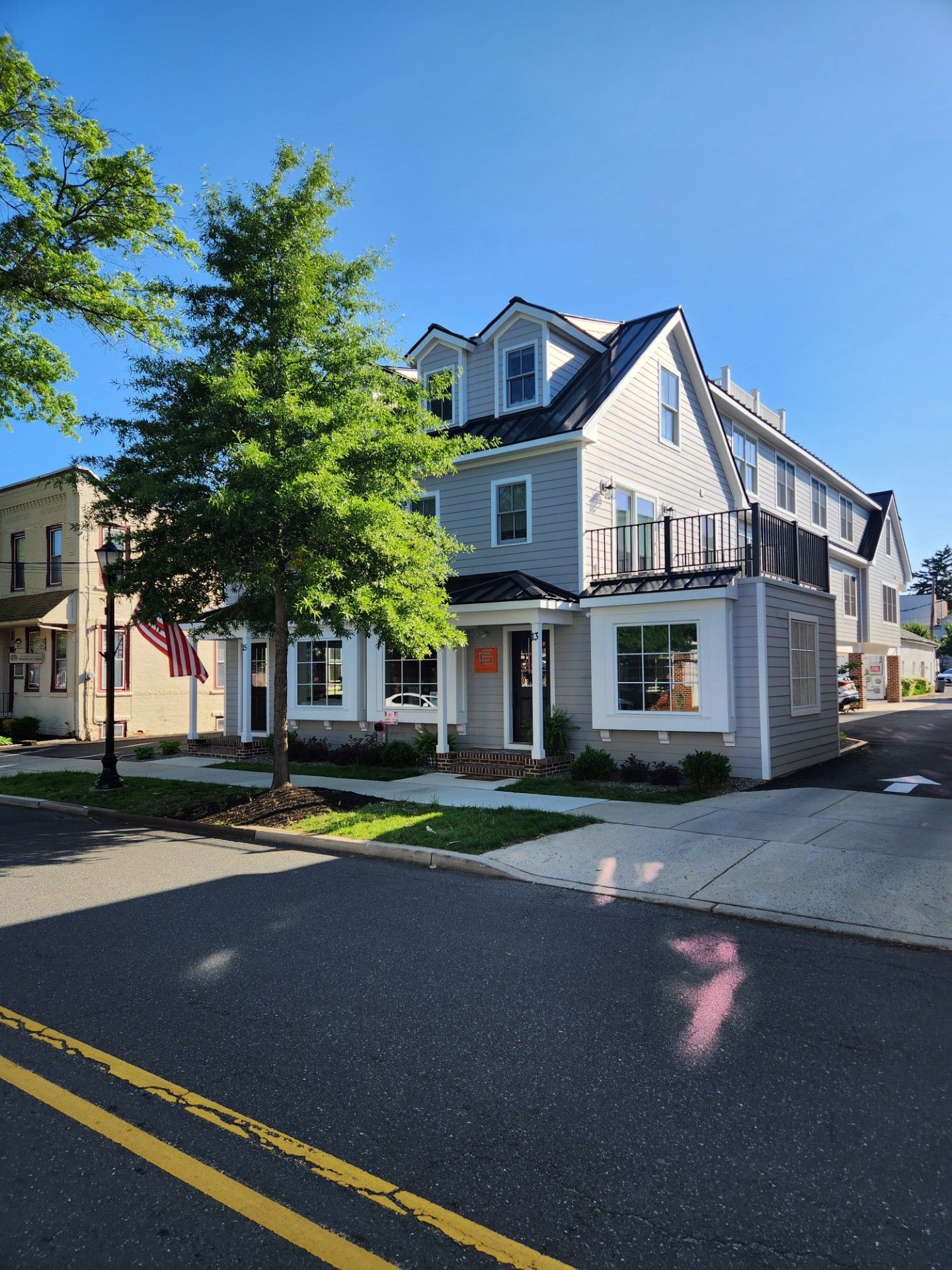 A white house with a balcony sits on the corner of a street.
