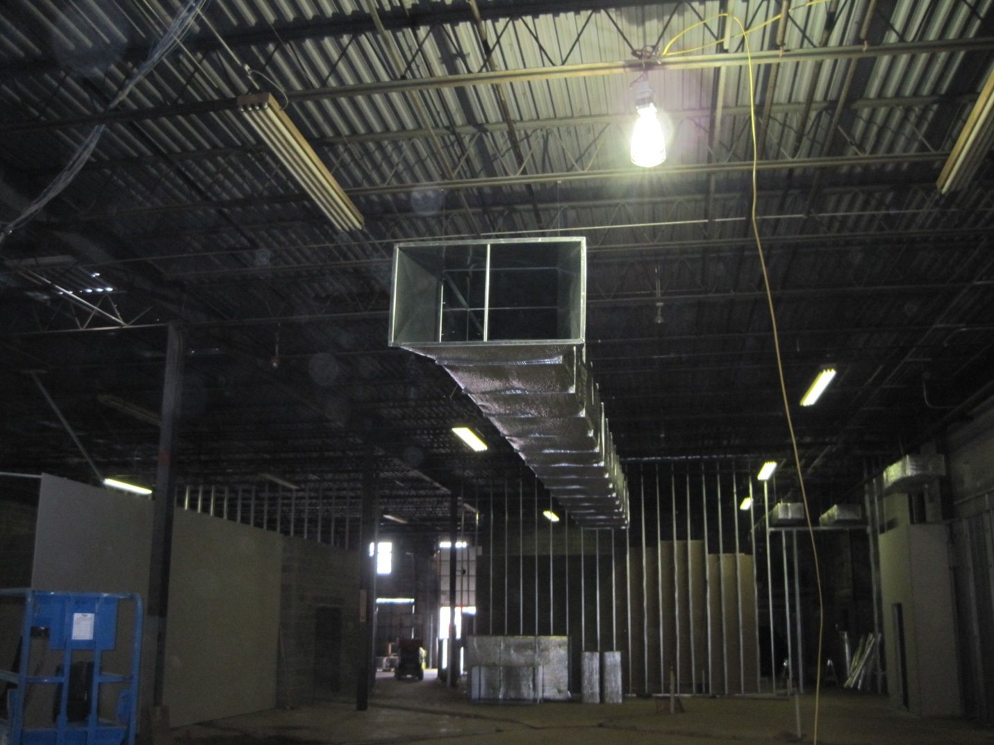 The inside of a building under construction with a large duct hanging from the ceiling.