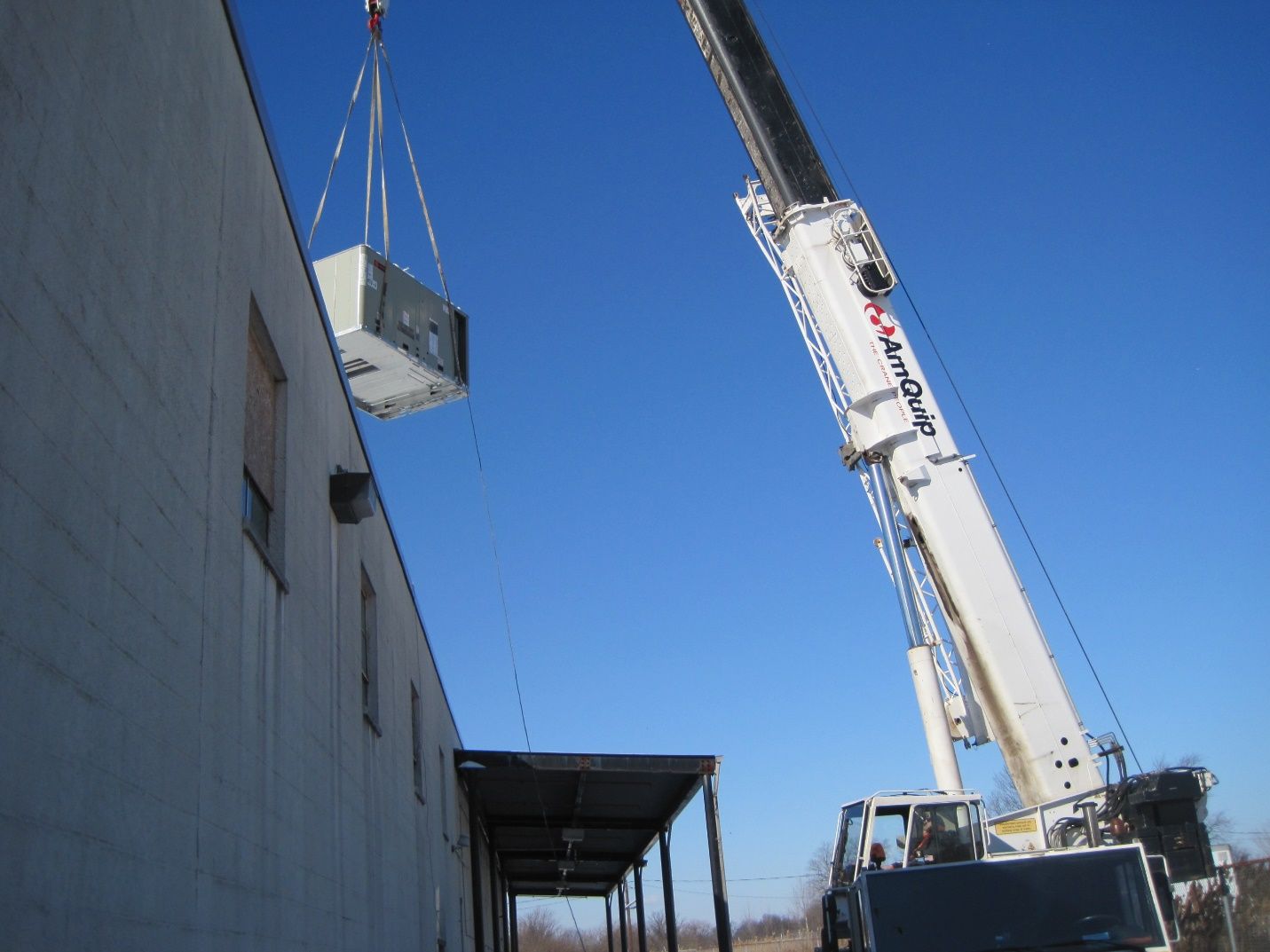 A large white crane is lifting a container from the side of a building.