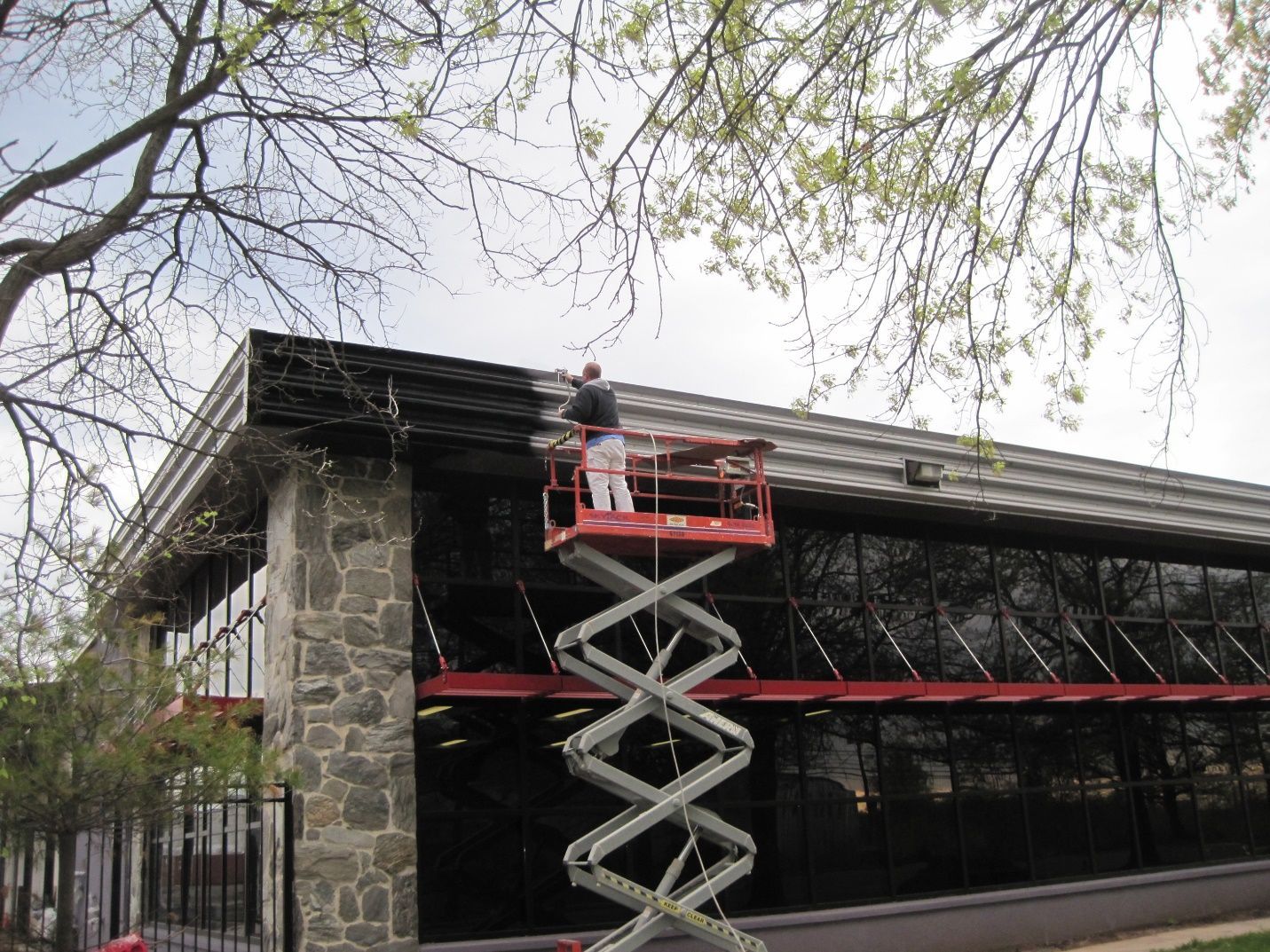 A man is painting the side of a building on a scissor lift.