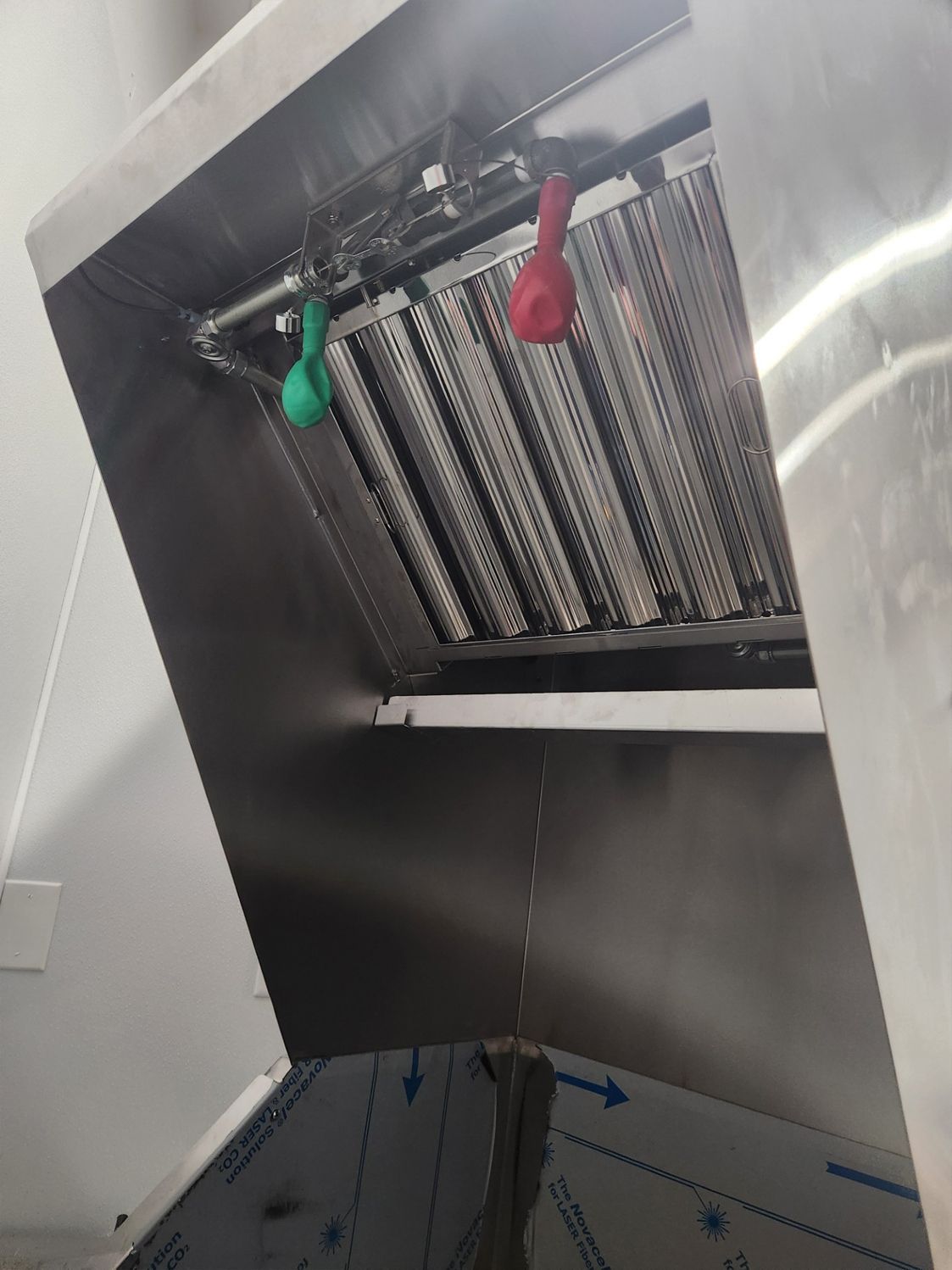 Inside of a commercial kitchen exhaust hood. The hood is silver with red and green balloons hanging from a sprinkler system.