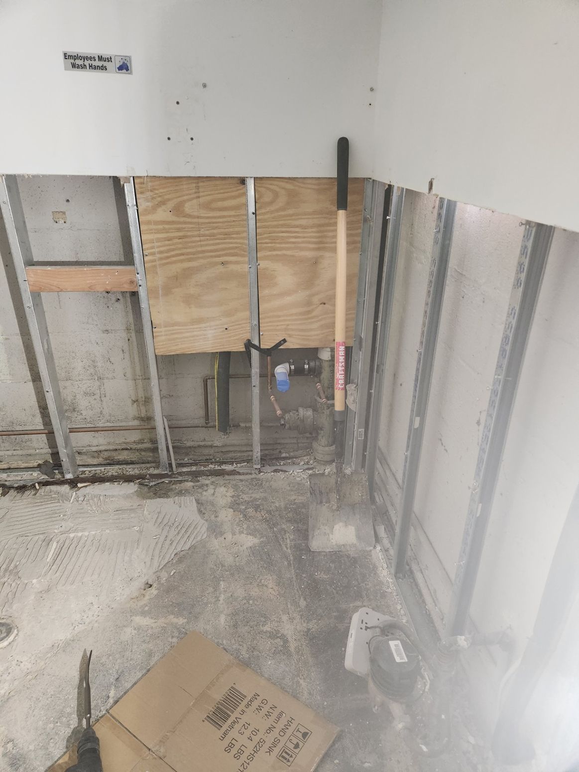 Construction site: exposed walls, plywood, tools, concrete floor, and a box.