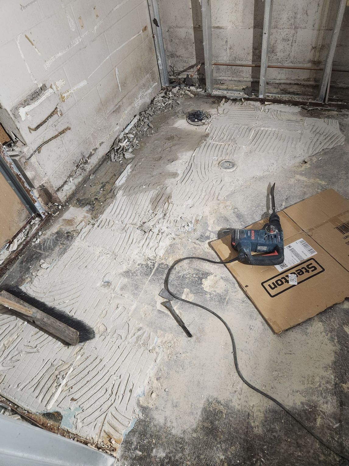 Bathroom remodel: demolition of tile and drywall; grinder tool on cardboard, debris on floor.