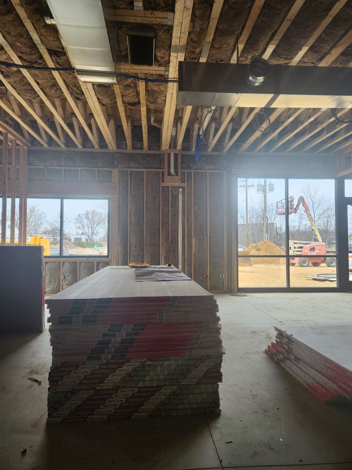 Interior construction site with stacked boards; wood framing, exposed ceiling beams, and windows.