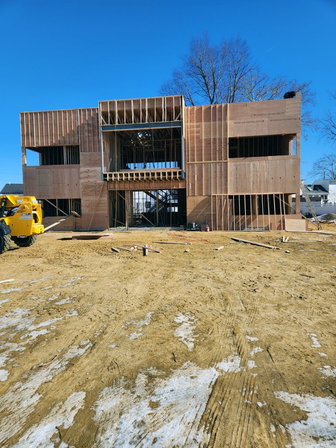 Wooden frame of a two-story building under construction on a dirt lot under a clear blue sky.