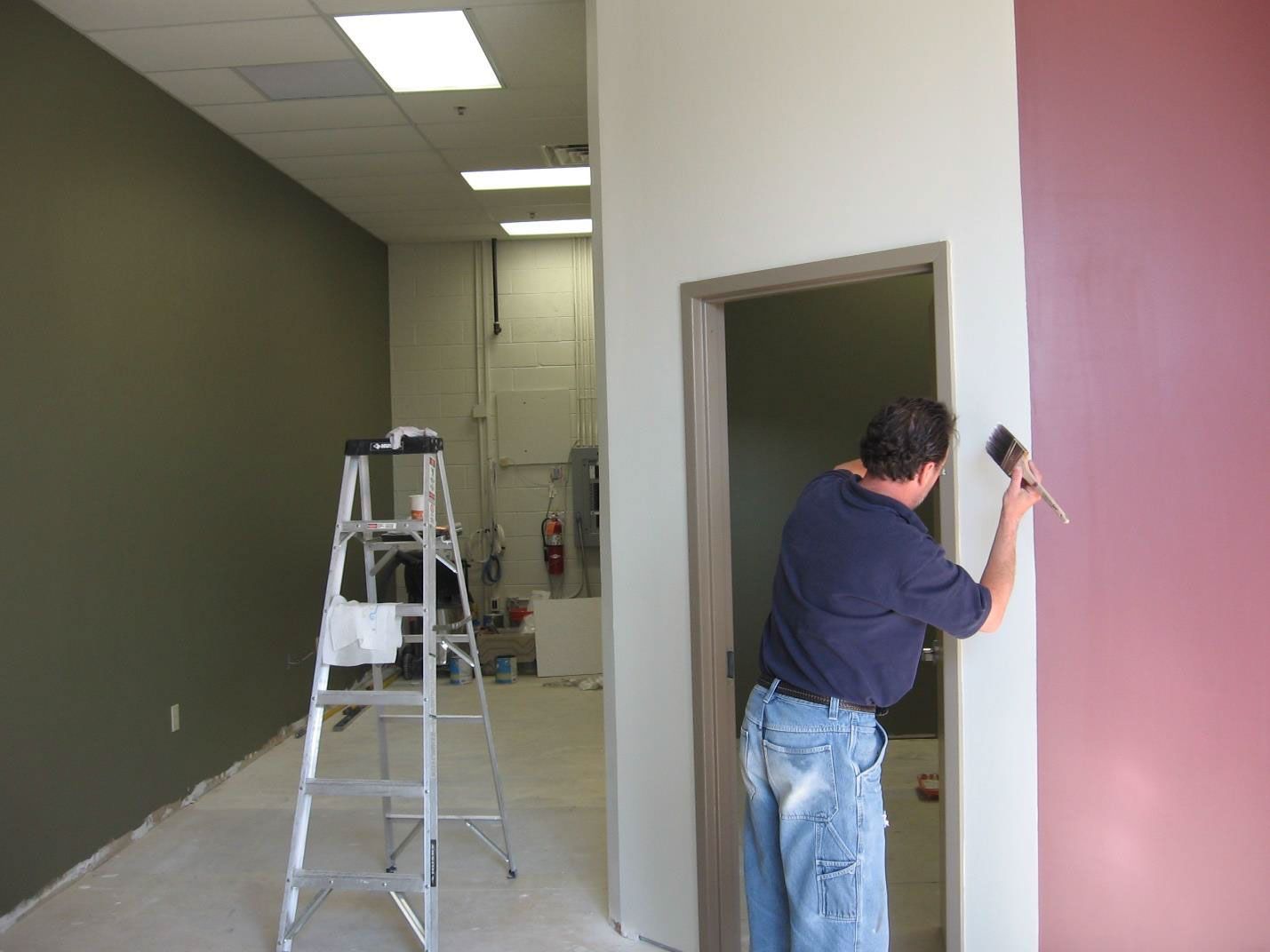A man is painting a wall in a room with a ladder in the background