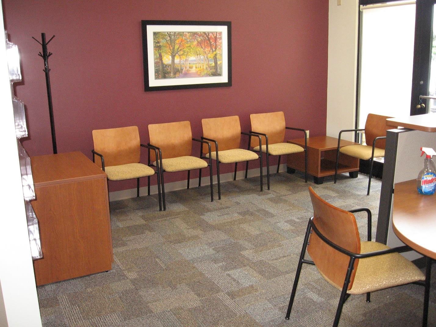 A waiting room with chairs, a table and a picture on the wall