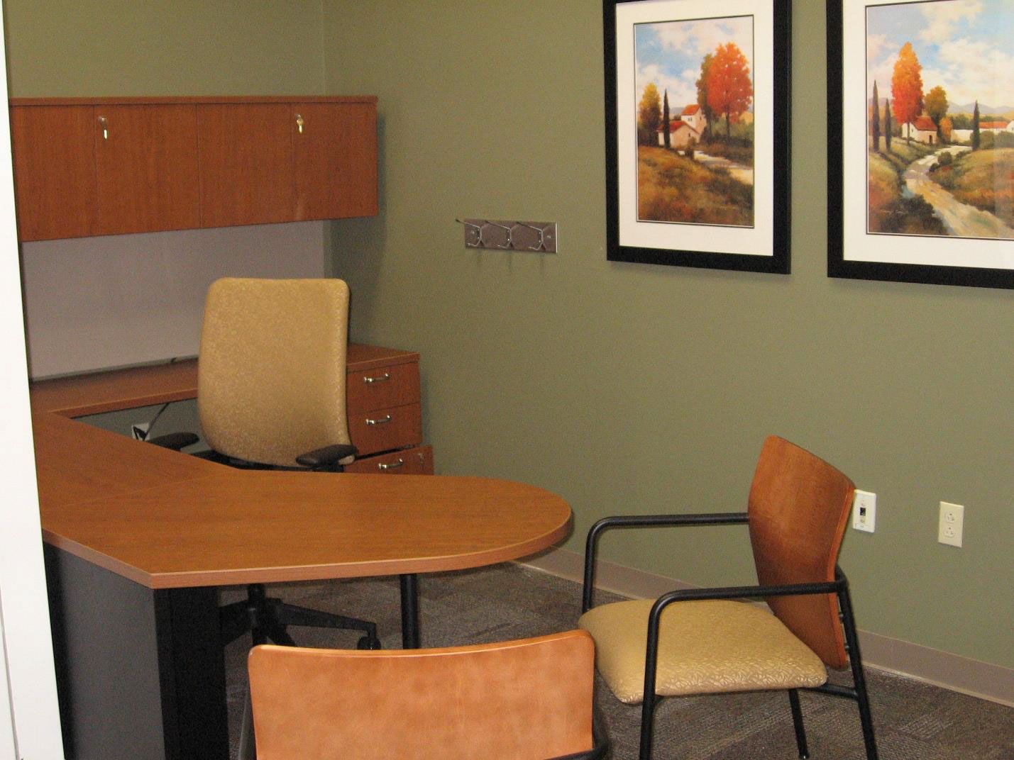 An office with two paintings on the wall above the desk