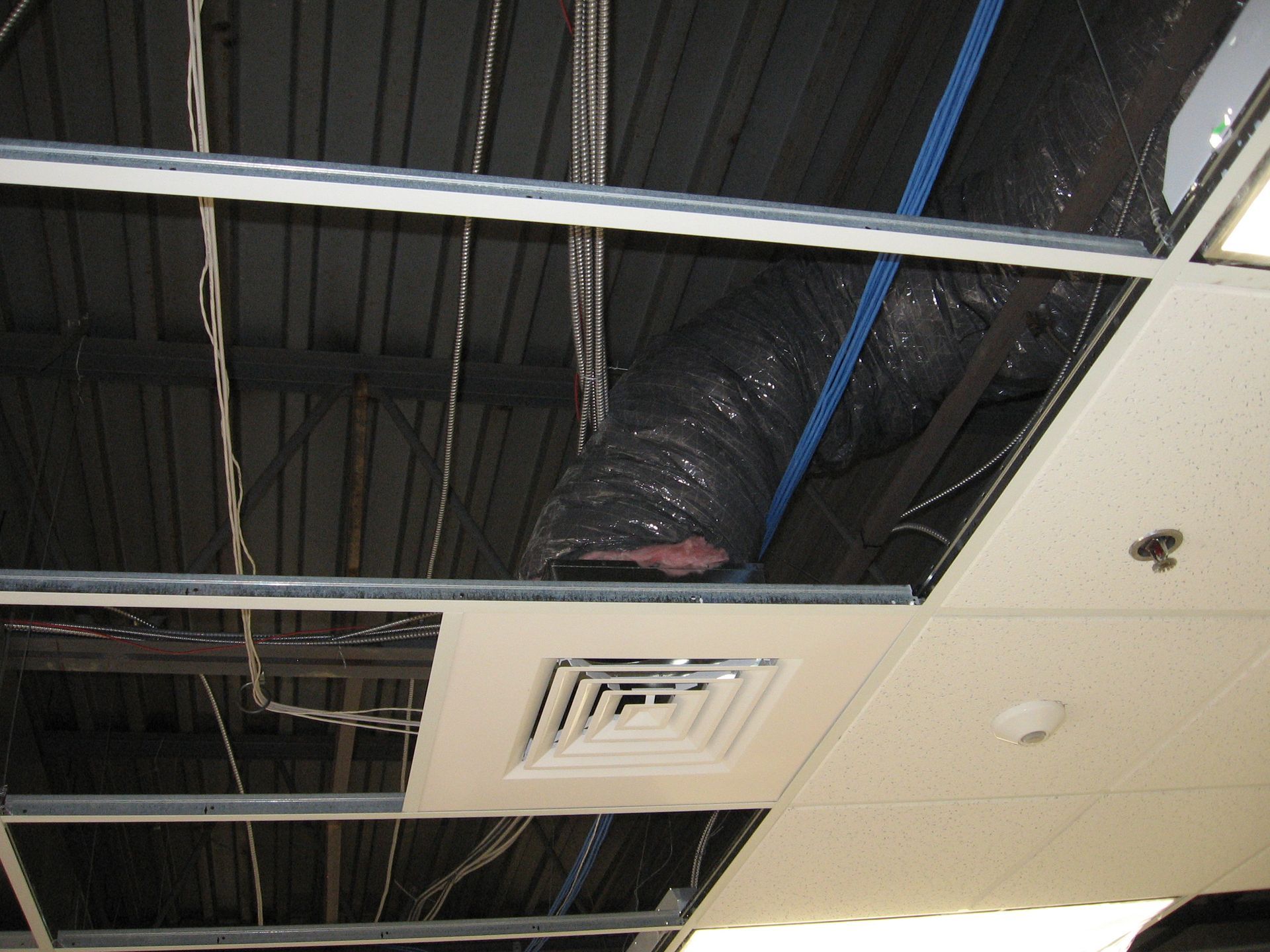 A ceiling with ducts and wires hanging from it
