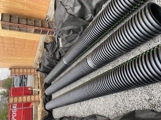 A row of black drain pipes sitting on top of a pile of gravel.